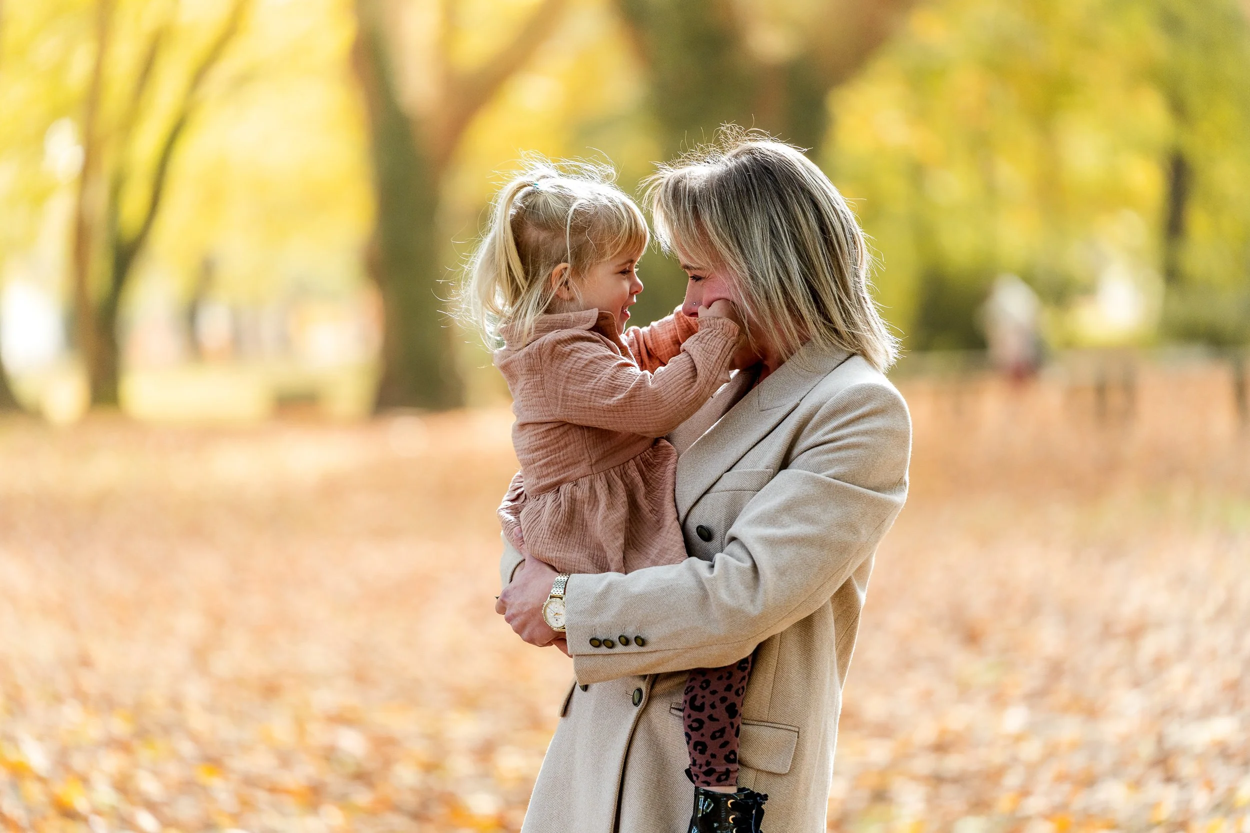 Eine Frau hält ein lachendes kleines Mädchen im Arm in einem Park mit herbstlichen bunten Blättern, im Hintergrund scheint die Sonne durch die Bäume der Ludwigshafener Parkinsel.