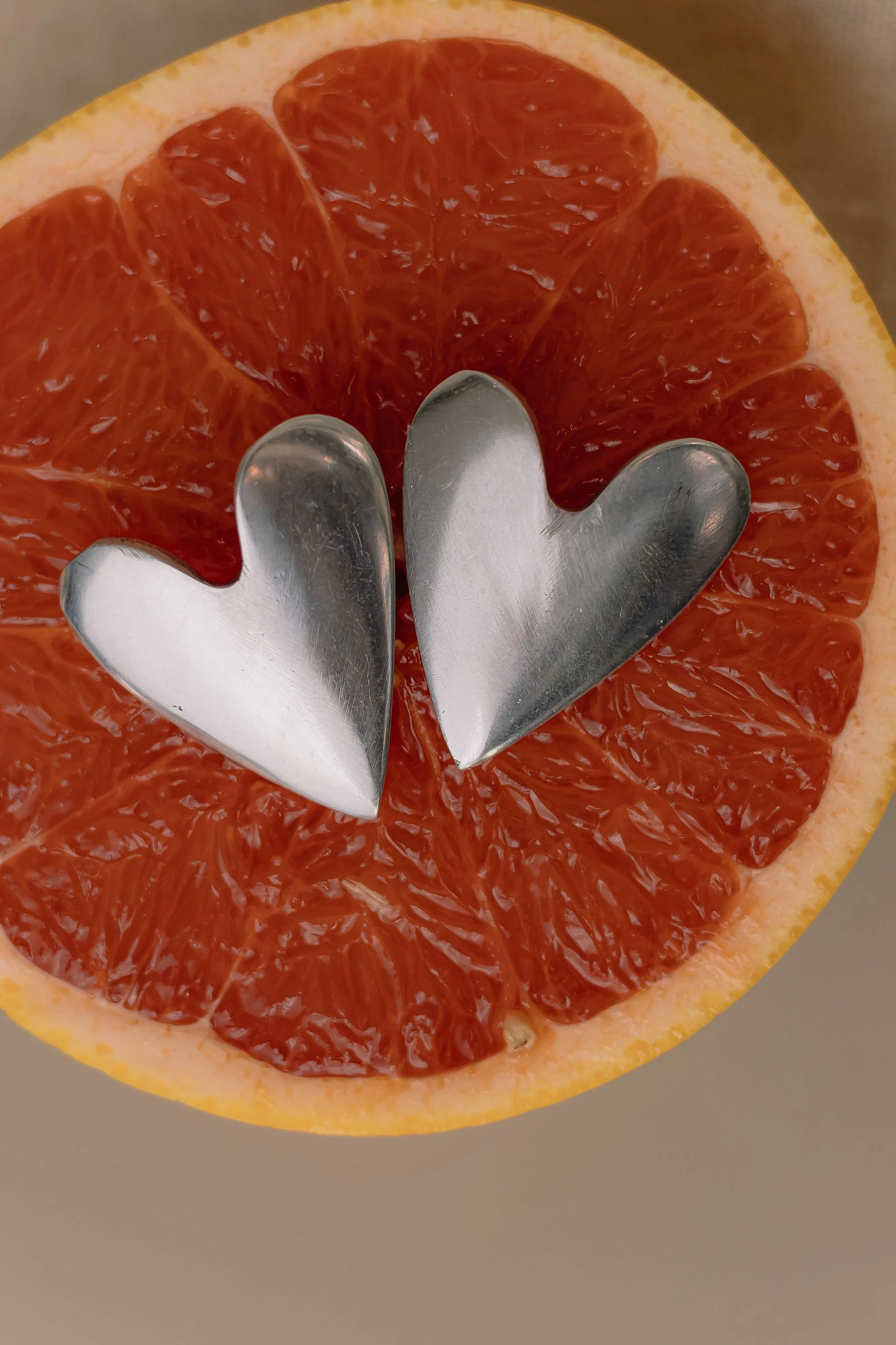 A halved grapefruit with two metallic heart-shaped utensils resting on top.