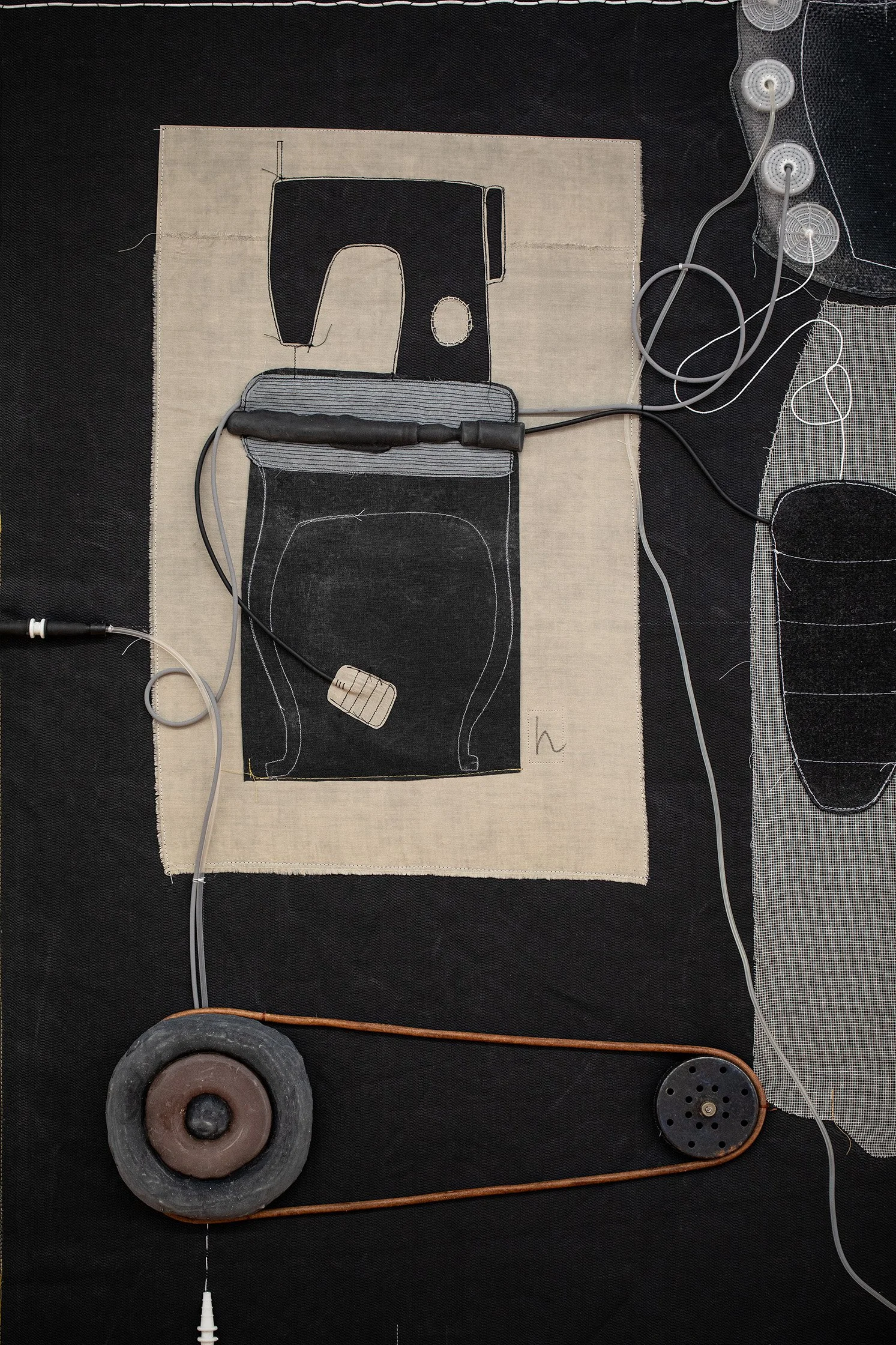 Kunstwerk von einer Nähmaschine auf Stoff, umgeben von elektrischen Kabeln und einem schwarzen Rad, das an ein kunstvolles mechanisches Objekt erinnert.