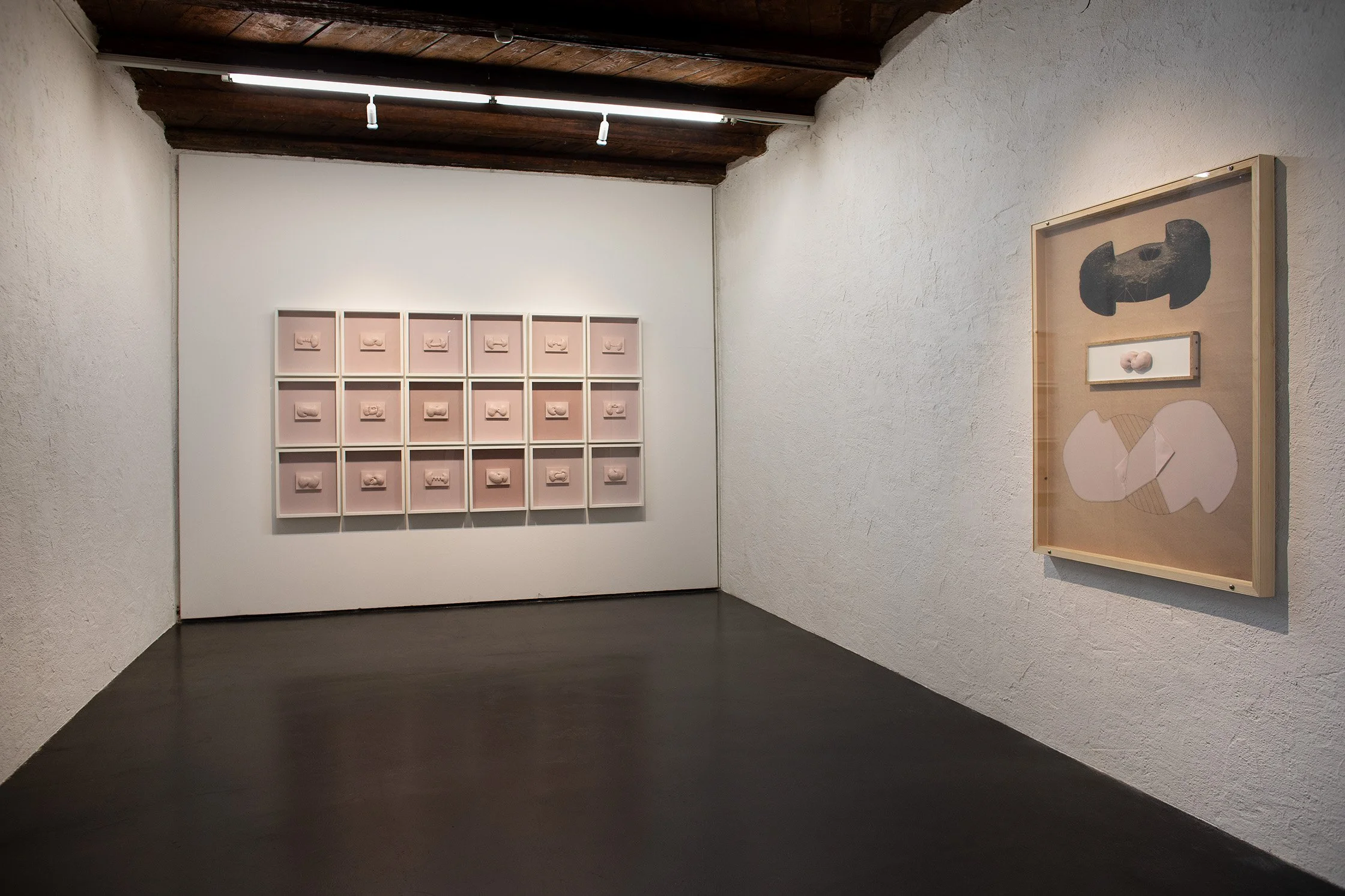 Kunstgalerie mit mehreren Miniaturkunstwerken in Rahmen an weißen Wänden und dunklem Boden.