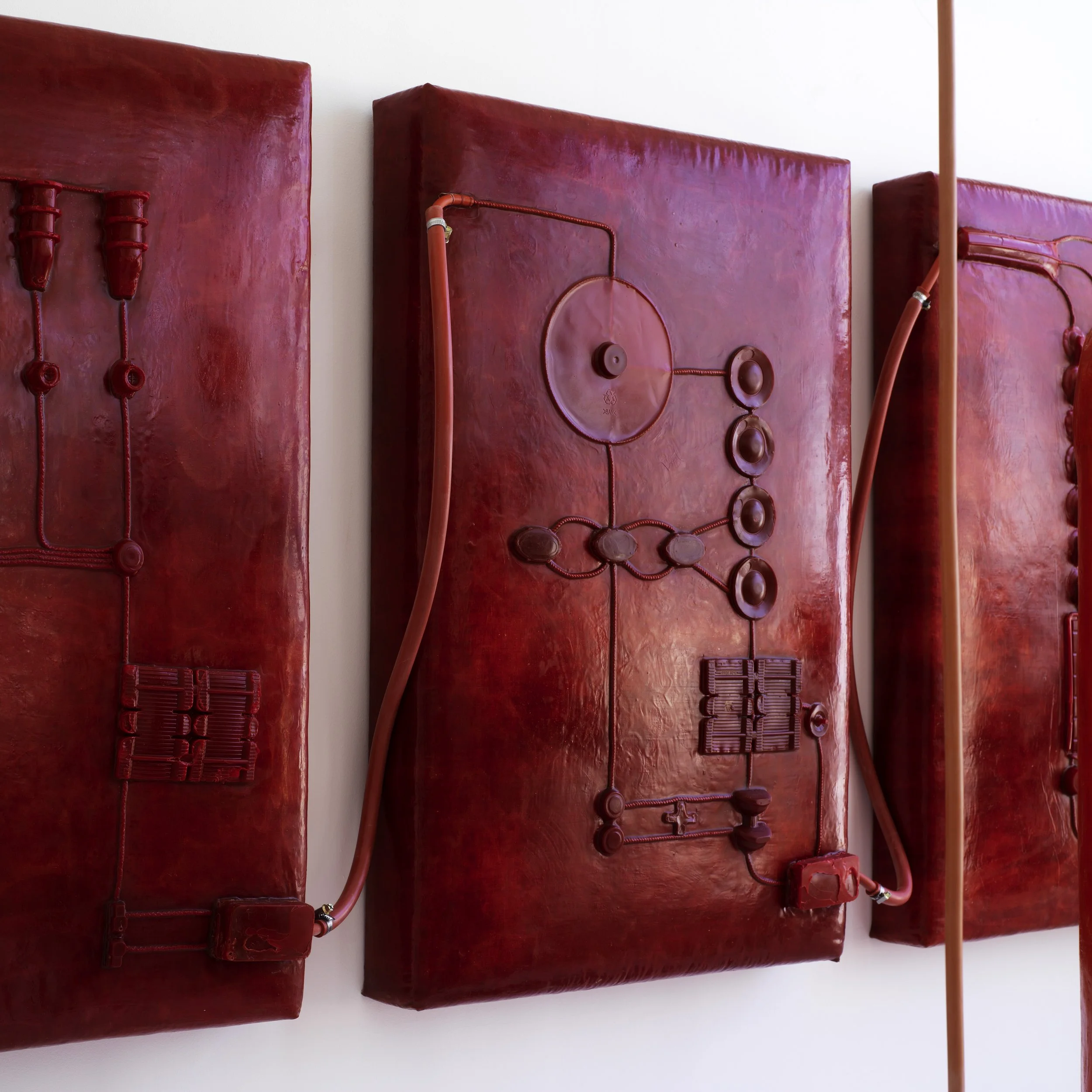 Kunstinstallation aus roten, industriellen Materialien, die an technische Komponenten erinnern, an einer weißen Wand befestigt.