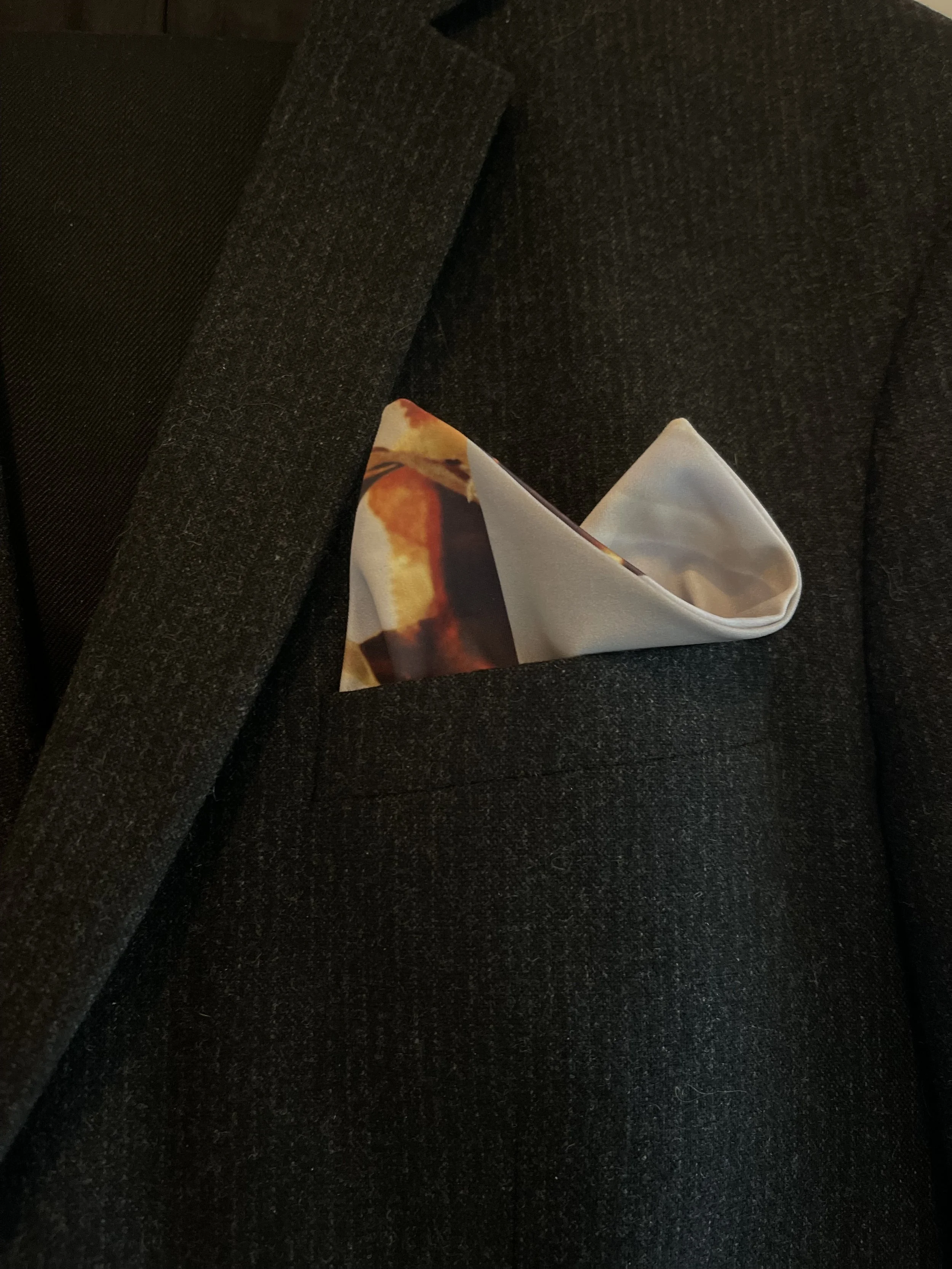 Close-up of a dark gray suit jacket with a patterned pocket square peeking out of the chest pocket.