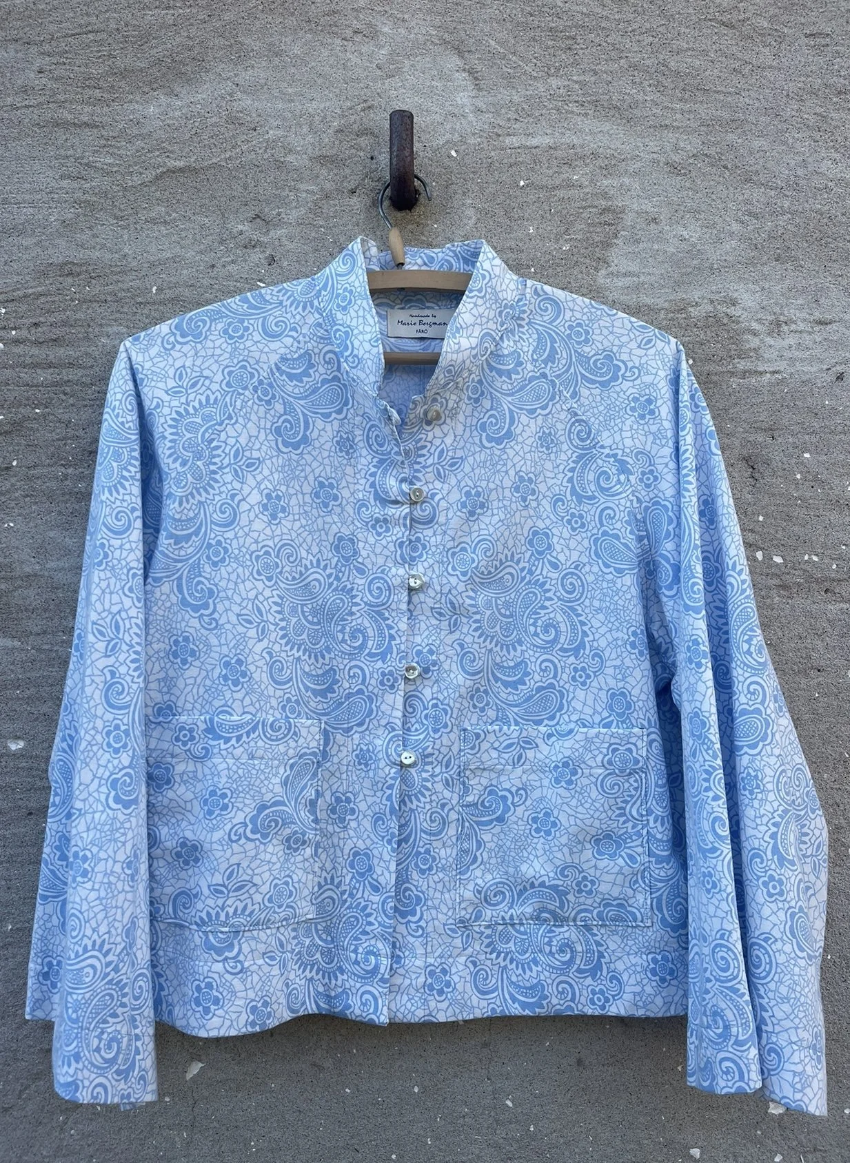 Blue and white patterned button-up shirt hanging on a hook against a concrete wall.