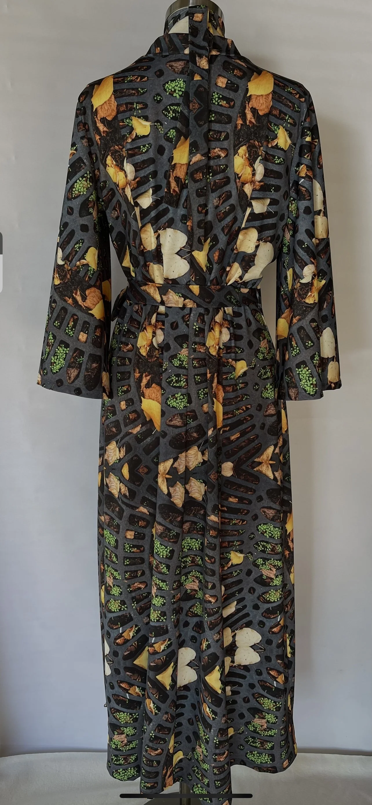 Black long dress with a colorful print of leaves, vegetables, and cutouts, featuring long wide sleeves and a belt at the waist.