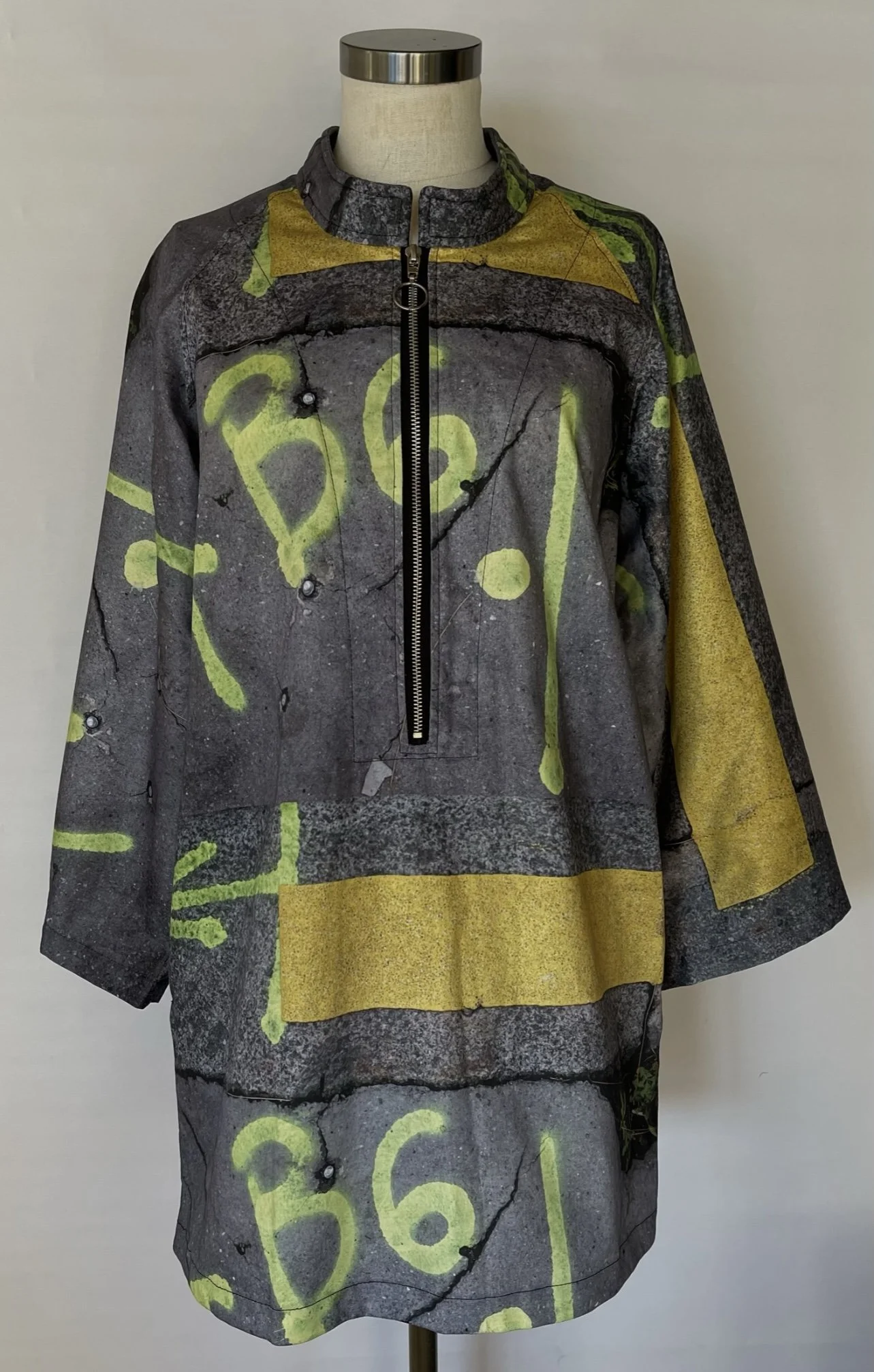 Long sleeve shirt with graffiti-style print resembling cracked concrete with yellow spray paint markings and a front zipper pocket.