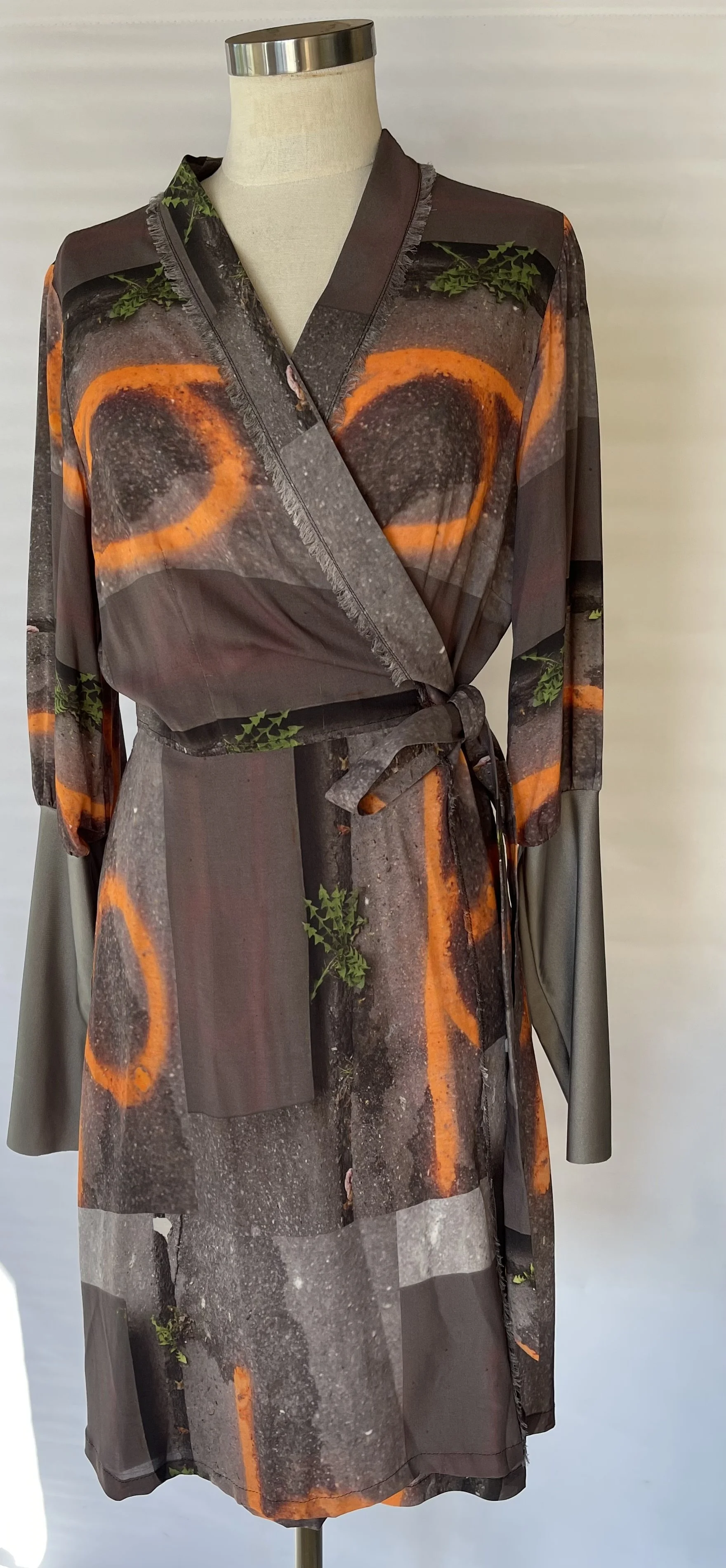 A women's dress with a print resembling a street scene with orange circles, graffiti, and green plants, displayed on a mannequin.
