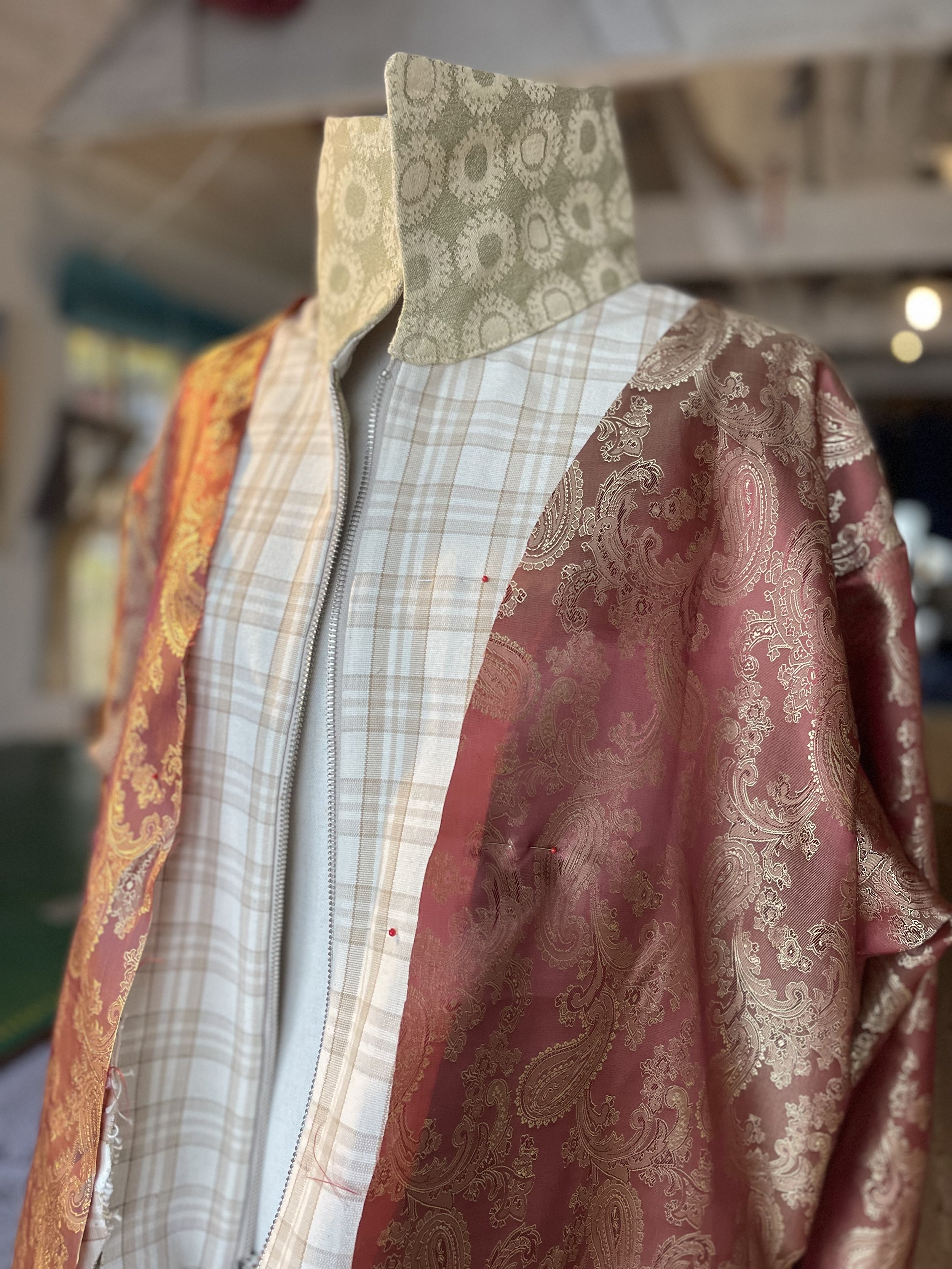 Close-up of a mannequin wearing a patchwork jacket with intricate paisley and floral patterns in shades of red, gold, and white, featuring a beige collar with a floral design.