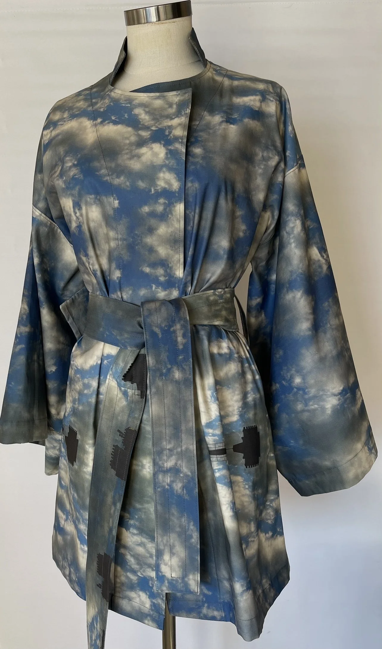 A coat with a sky and cloud pattern displayed on a mannequin.