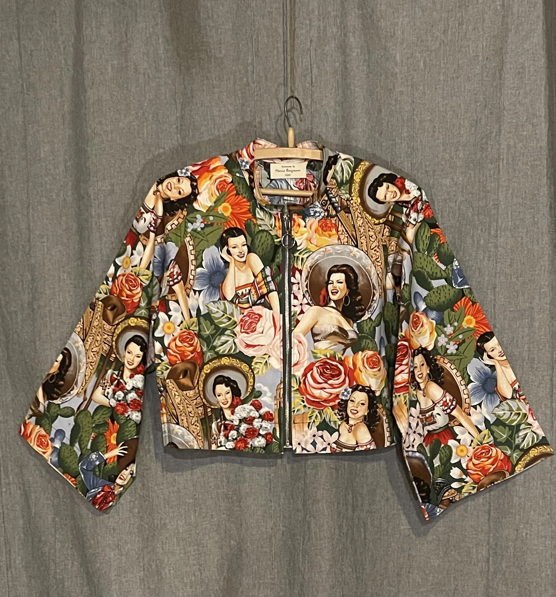 Colorful jacket with vintage pin-up girl illustrations and floral patterns, hanging on a wall.
