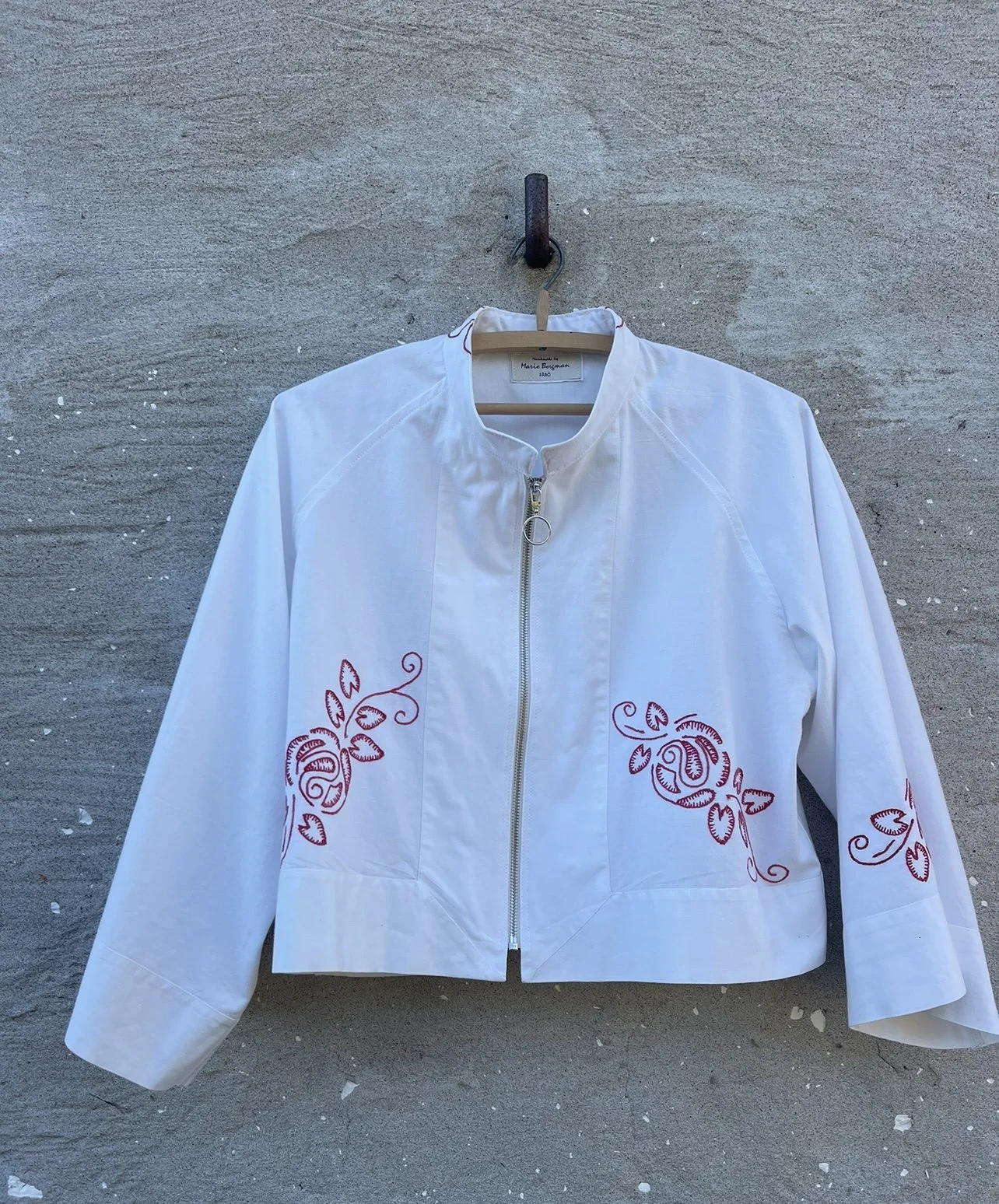 White jacket with red embroidered floral designs hanging on a wall.