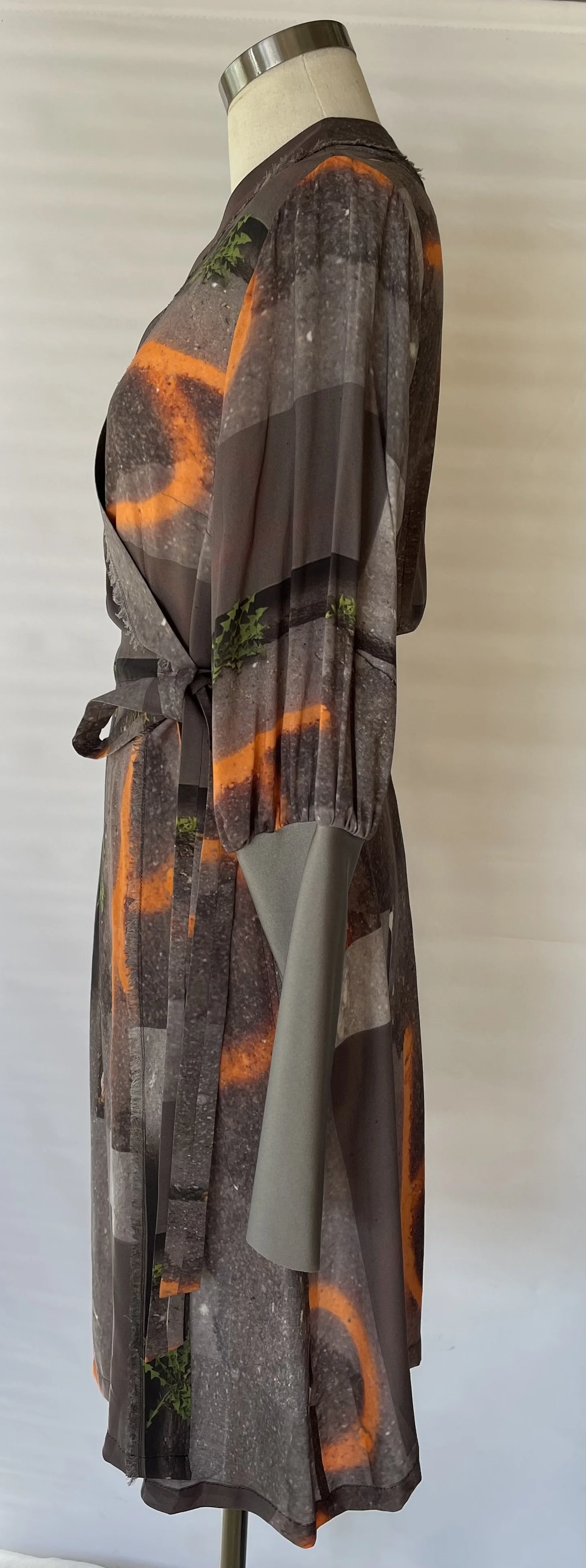 Mannequin dressed in a silk or satin robe with a graffiti-inspired print of orange circles and green leaves, standing indoors against a plain white background.