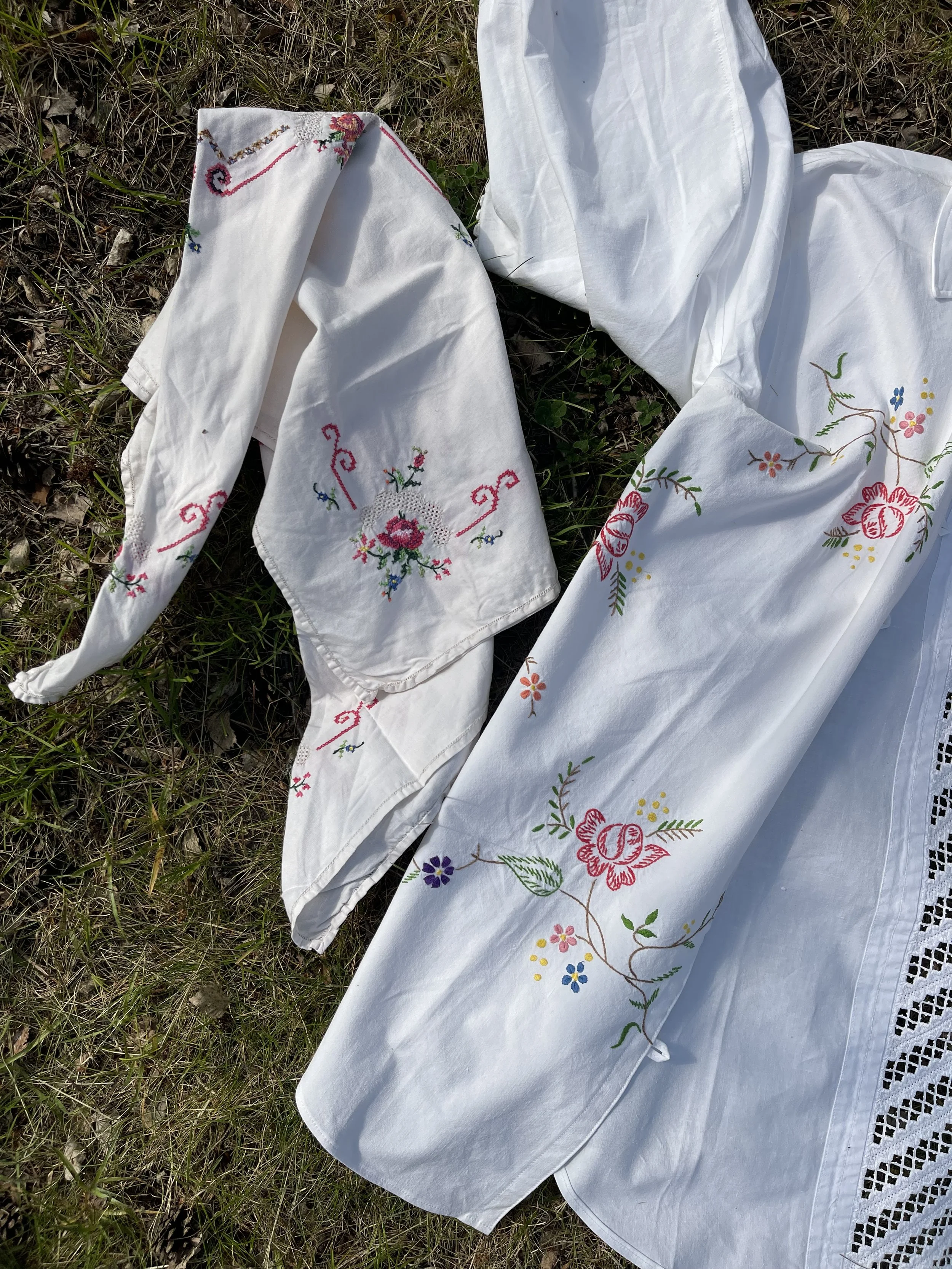 White embroidered linen with colorful floral patterns, lying on grass.