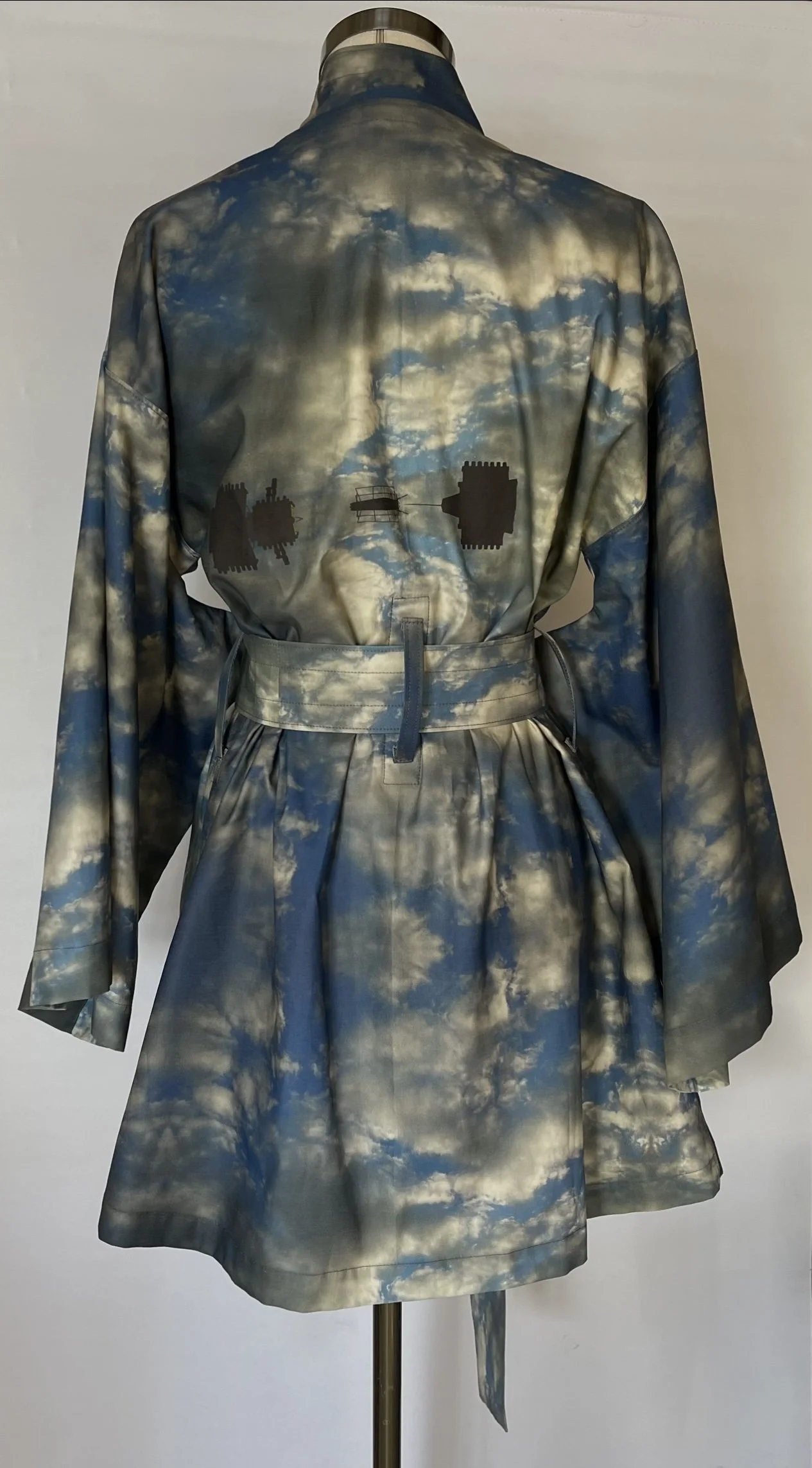 A garment with a sky and clouds pattern, featuring silhouettes of industrial structures on the back.