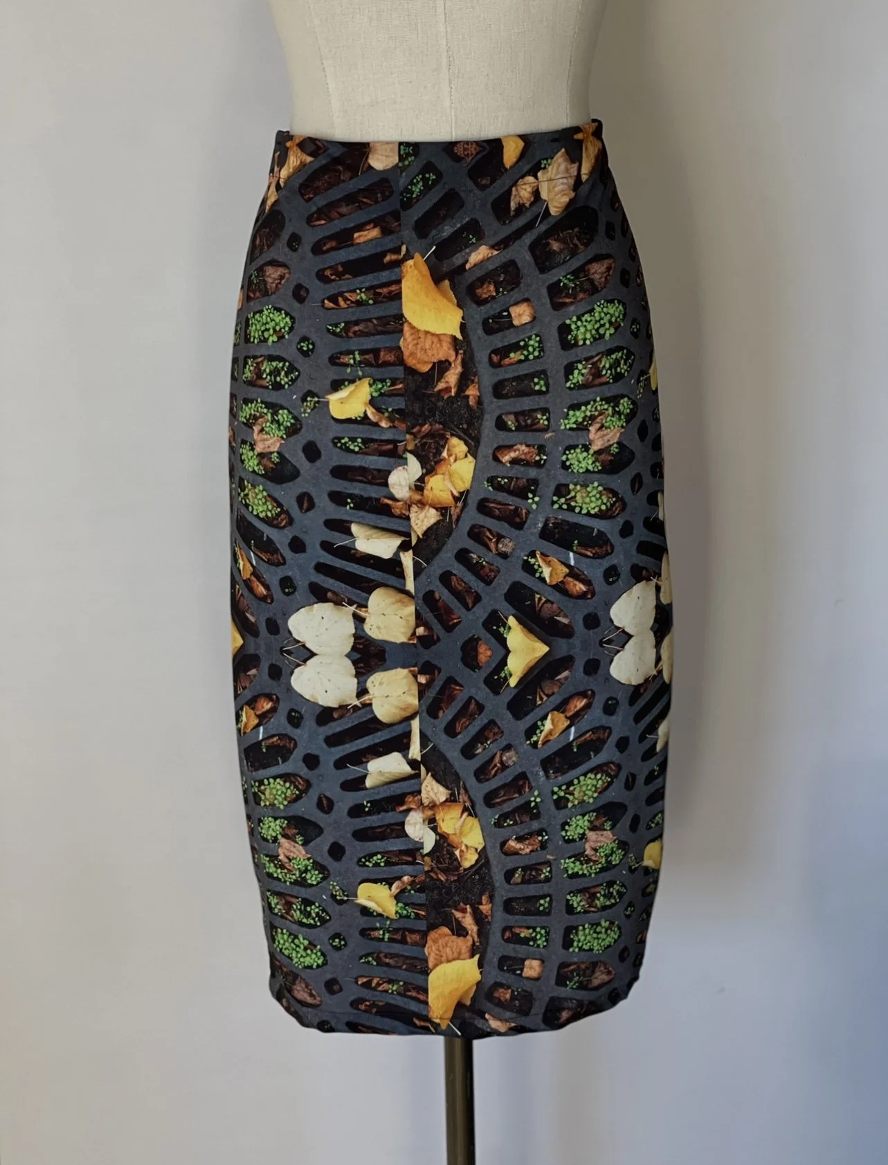 A skirt on a mannequin with a botanical pattern featuring leaves and green buds on a black background.
