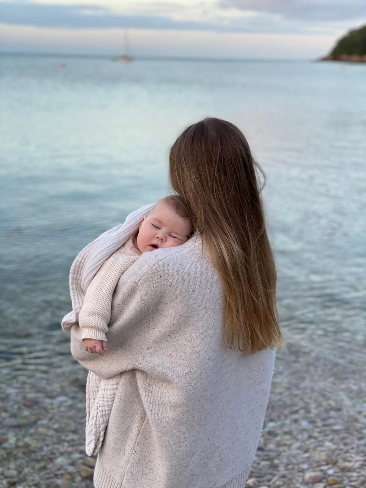 Postpartum mum and her baby surrounded by the ocean, hugging and relaxing on the beach