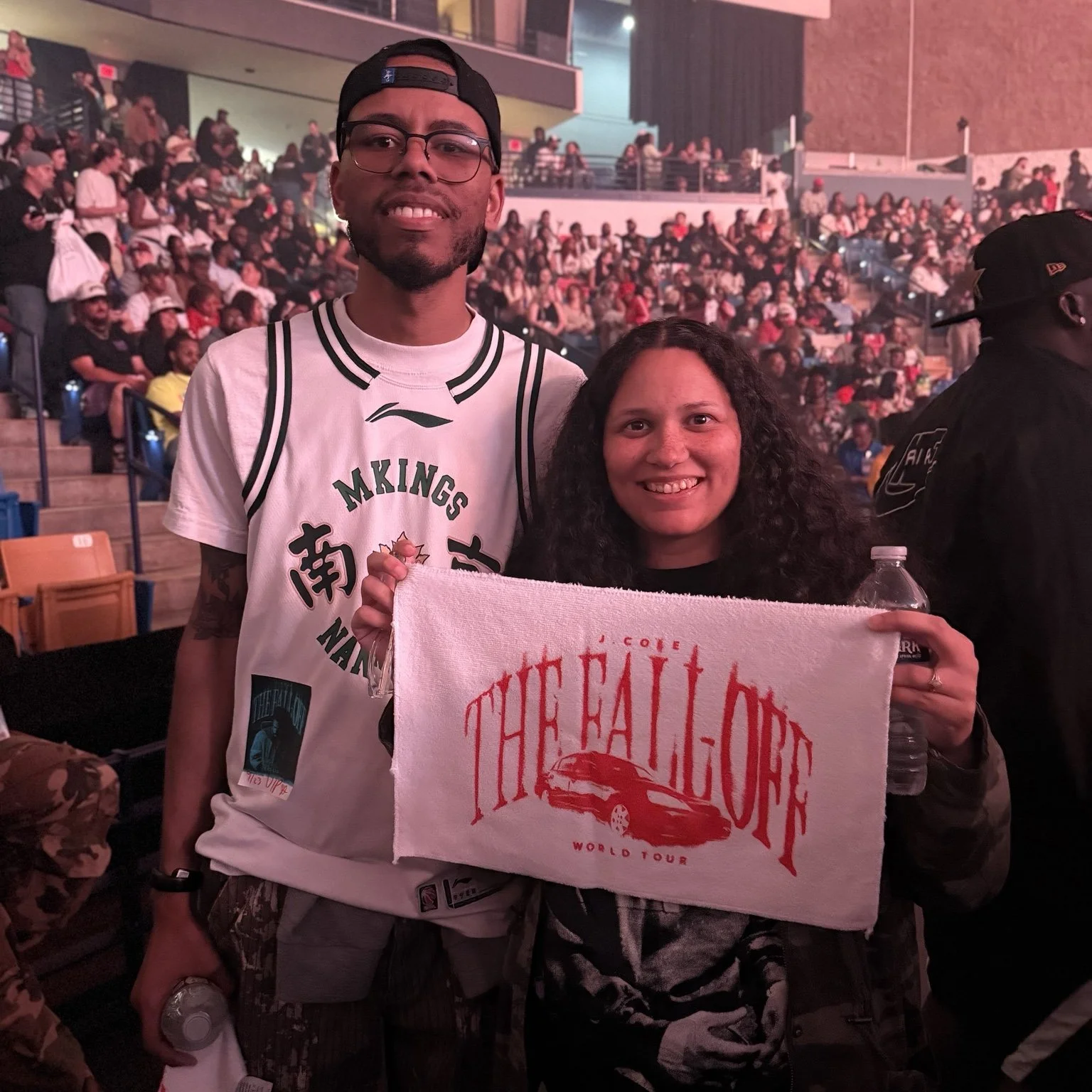 DaQuan and a companion smiling in the arena while holding a The Fall-Off World Tour towel.