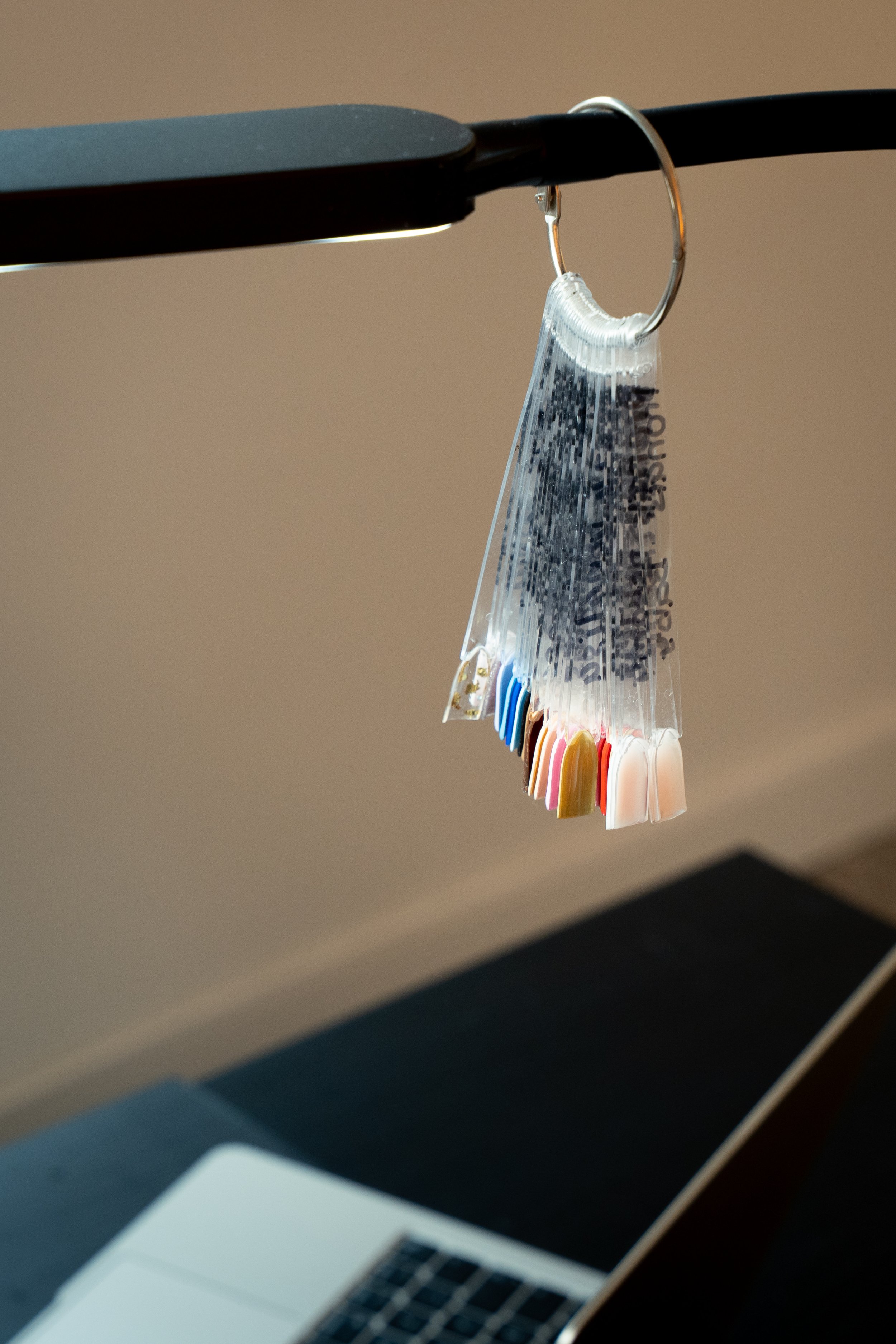 Een kleurstaalwaaier met verschillende kleuren nagellak op een bureau, met een laptop op de achtergrond.