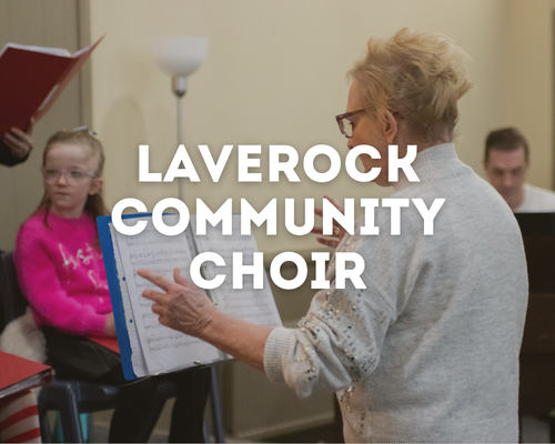A woman teaching a children's choir class, with a young girl in a pink shirt and glasses, and other children in the background.