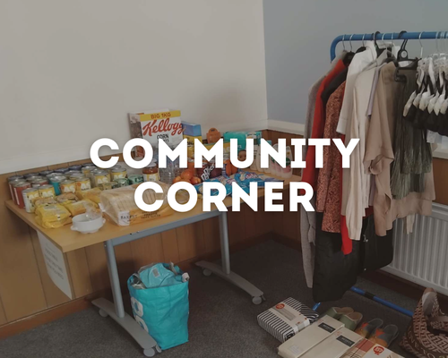 Table with canned goods, boxed food, and cereal, next to a rack of clothing in a community corner.