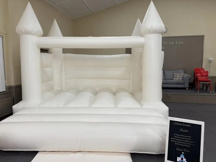 Inflatable white castle-themed bounce house with towers, set up indoors for a kids birthday party hall hire.