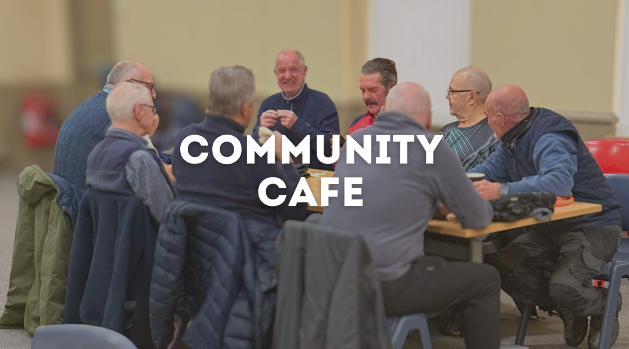 A group of older adults sitting around a table in a community cafe, smiling and engaging in conversation.