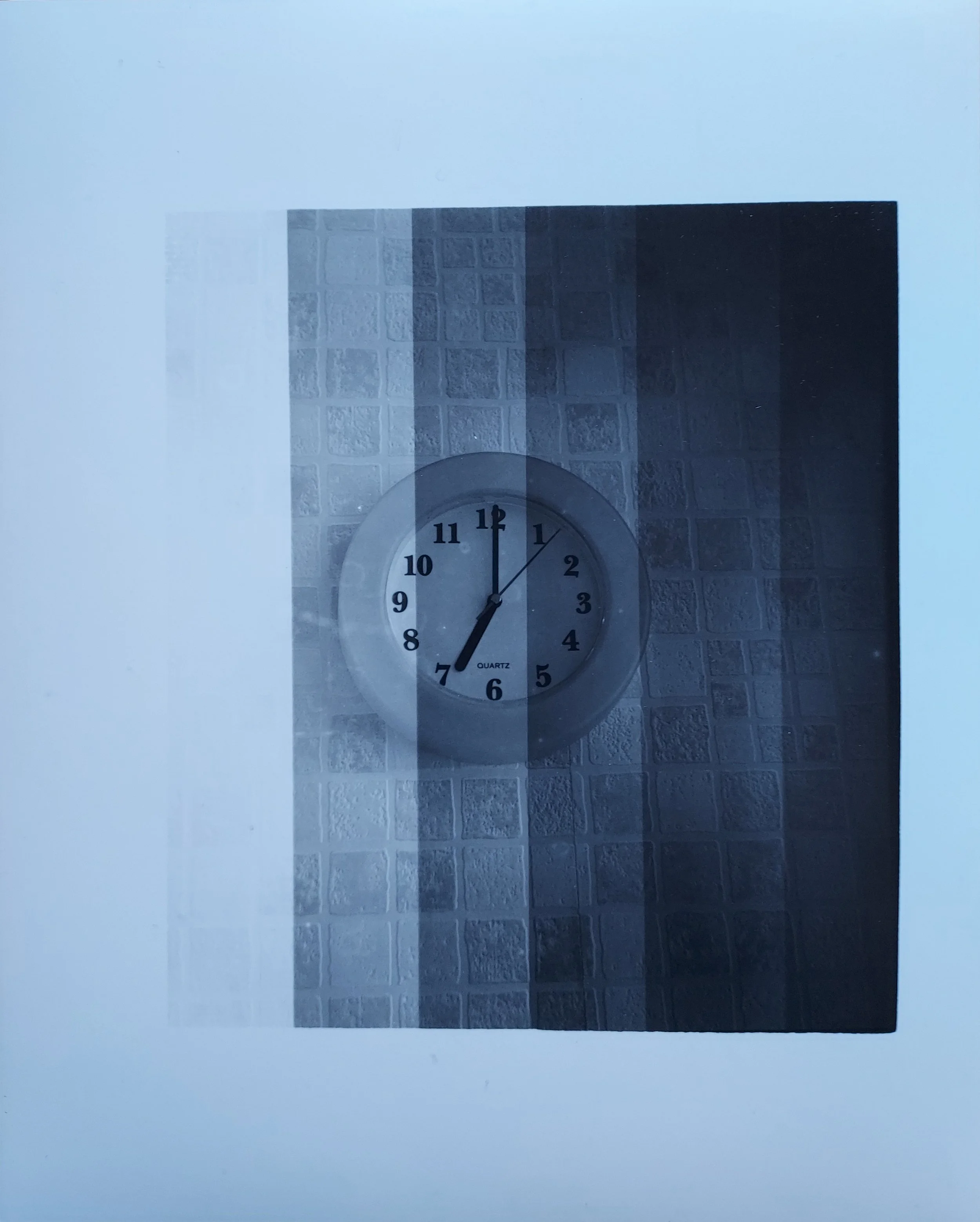 7 Seconds (2023)
Analogue photograph of a clock saying 7 seconds past 7o’clock. Hand printed in the darkroom.  The paper was exposed in intervals of 1 second, seven times, to produce the difference in exposure in the image.