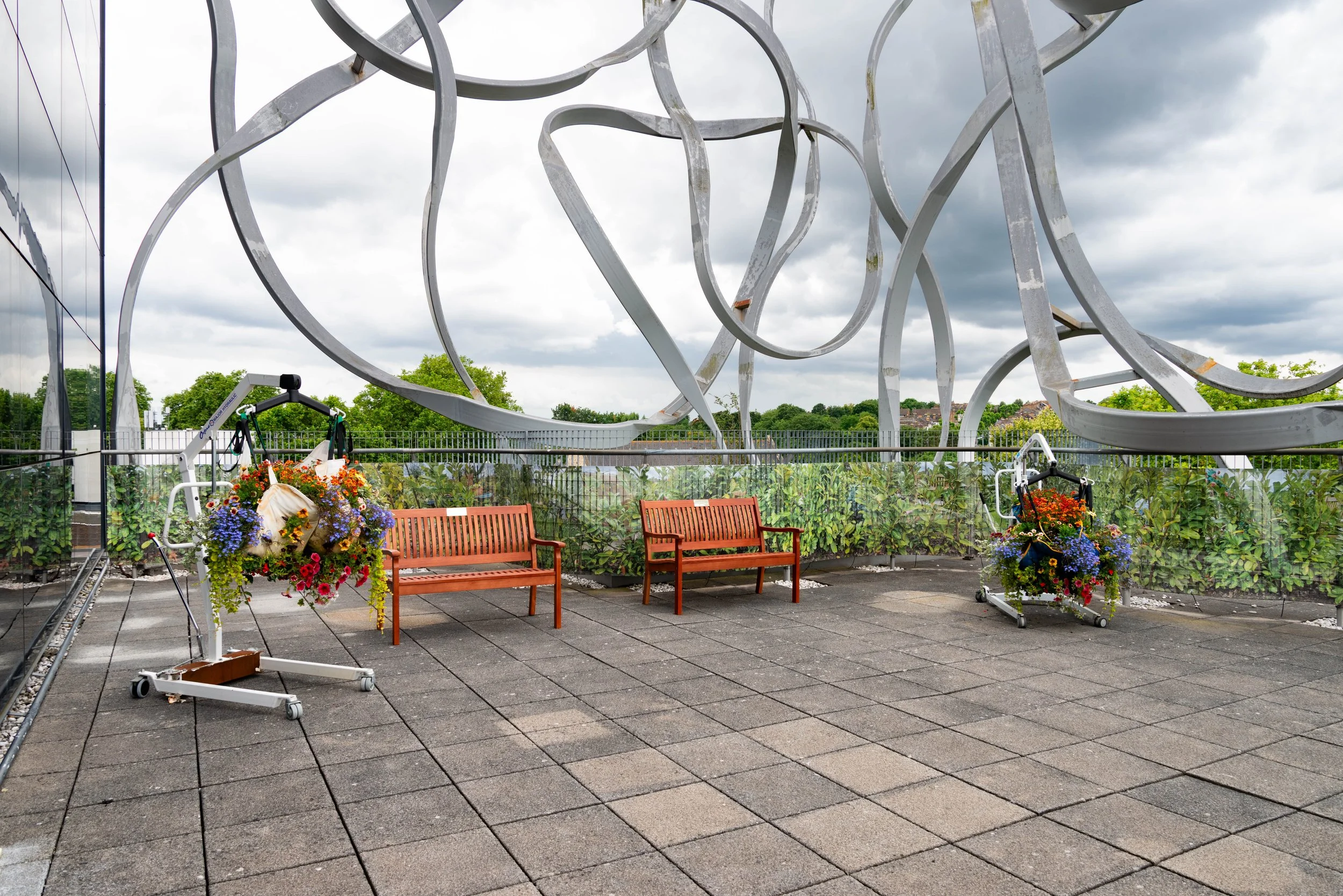 Ben Pimlott Terrace Goldsmiths College Degree Show 2024.
Patient hoists & slings.
Compost from my kitchen & garden waste (2019-2023) to the weight of their bodies.
Bedding plants.

Two Benches & Plaques

Cemetery Hedge
Digital photographic montage pr