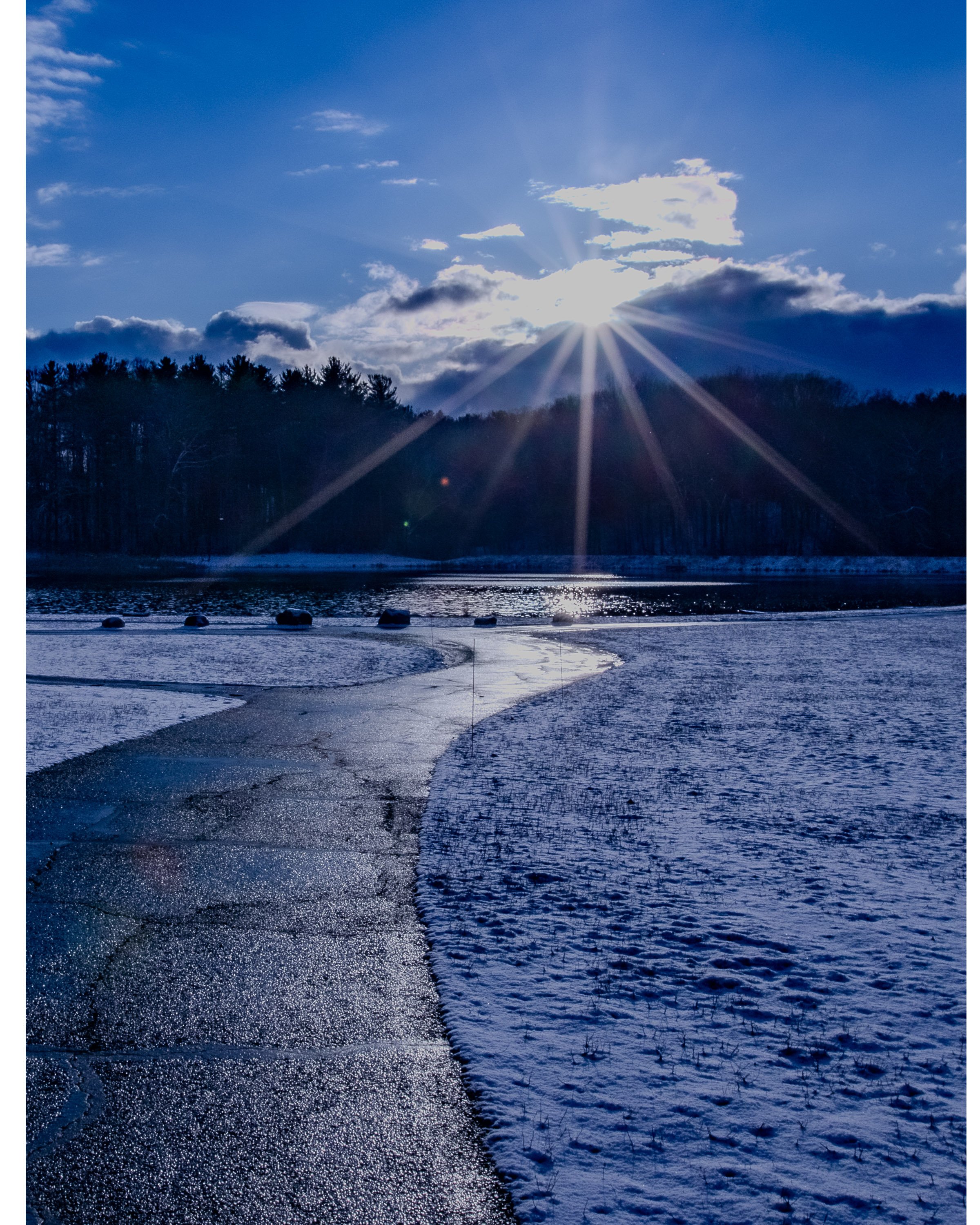 Sunlight breaking through clouds over a frozen shoreline, peaceful winter landscape fine art photography