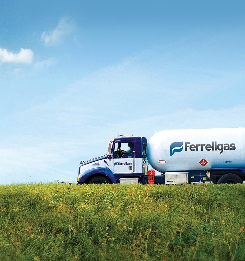 A blue and white propane delivery truck with the logo "Ferrellgas" on the side, parked on a grassy hill under a partly cloudy sky.