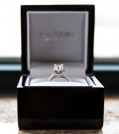 A diamond engagement ring in a black jewelry box on a windowsill.