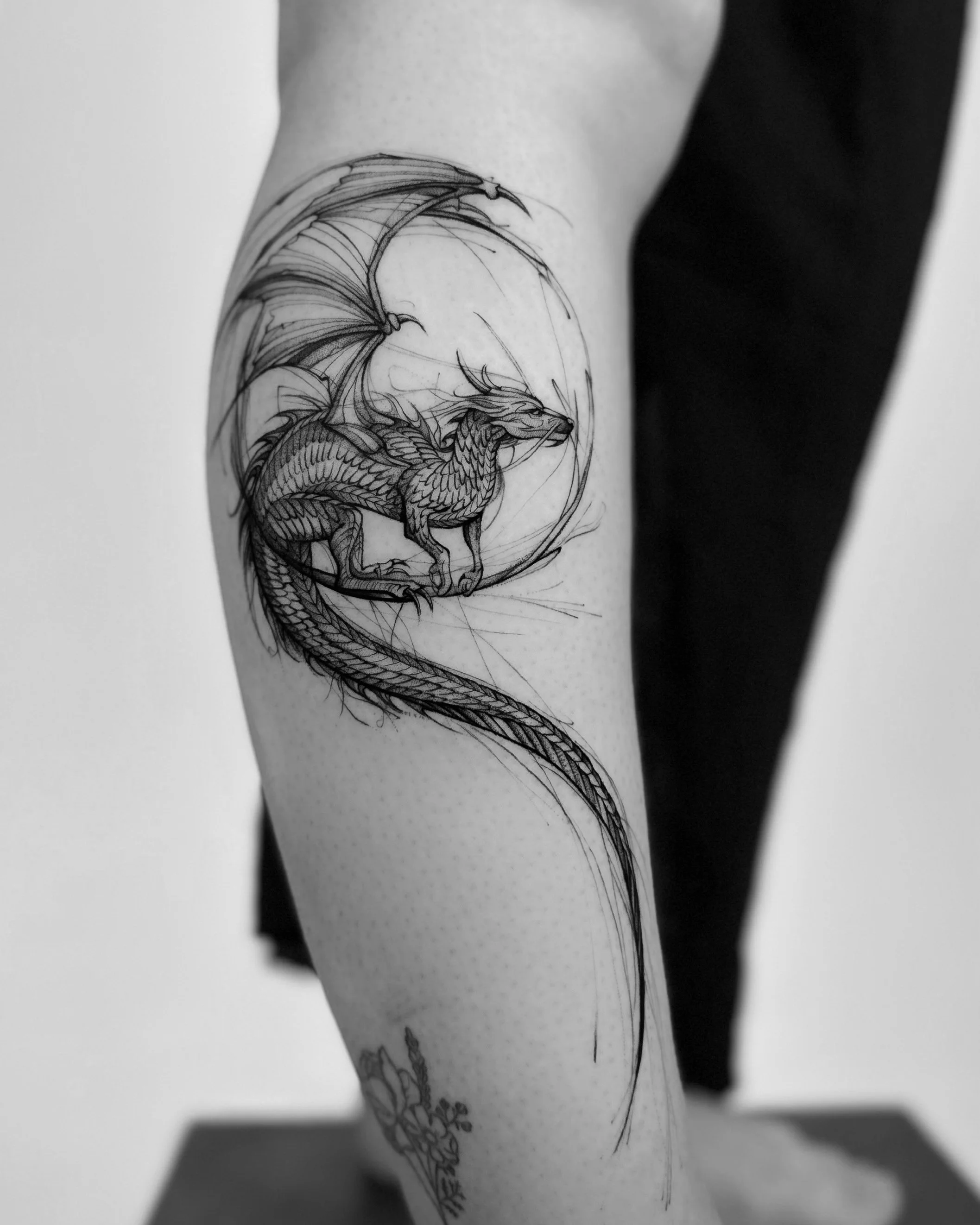 Black and white tattoo of a dragon on a person's thigh.