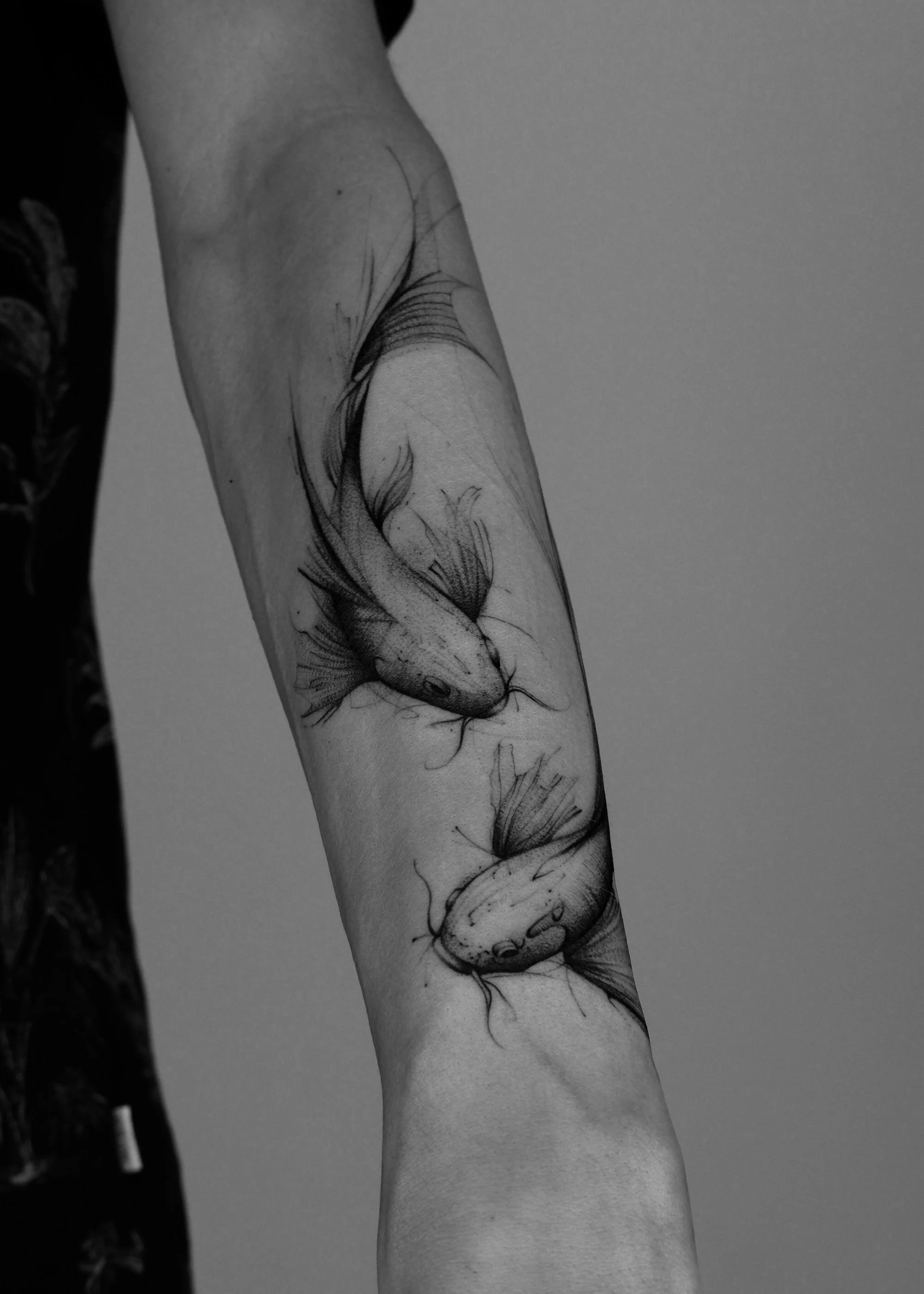 Black and gray tattoo of a fish swimming upward on a person's forearm.