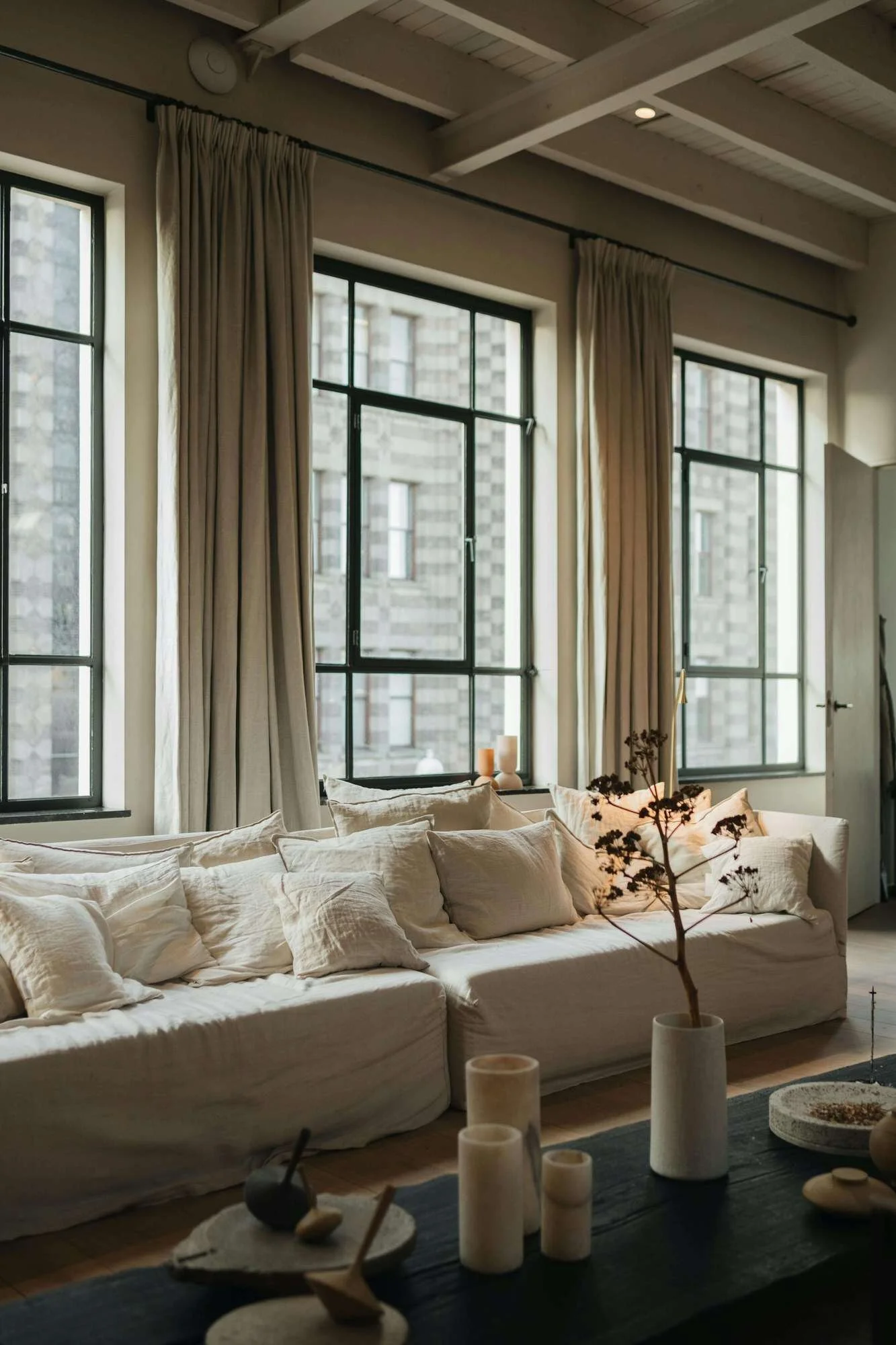 Real Estate DevelopmentConsultant - licing room with cream couch, 3 windows with black panes and beige curtains, overlooking the city