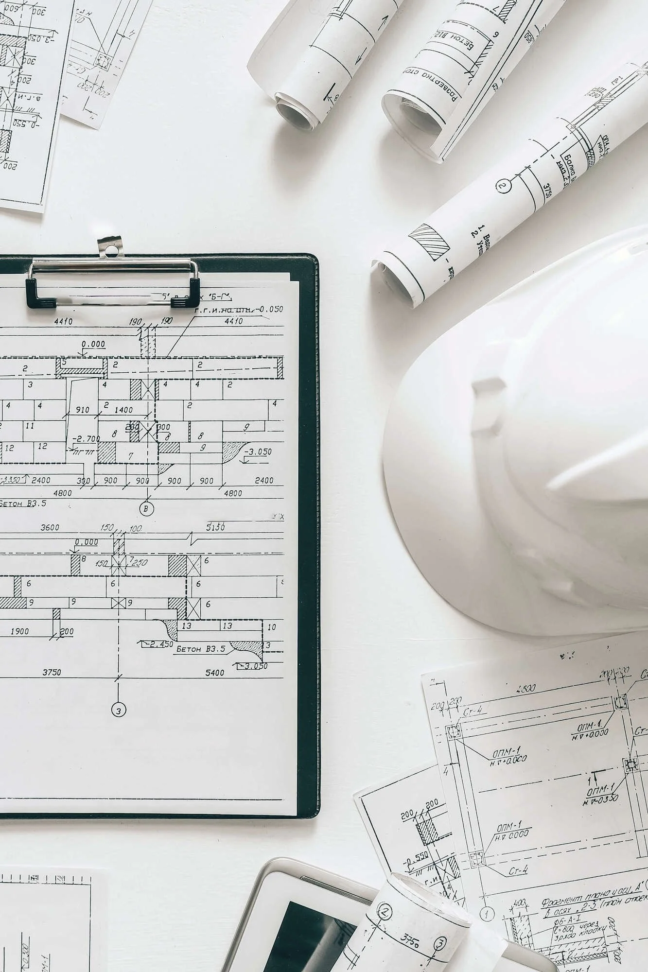 white table, with white hard hat, black clip board holding project plans