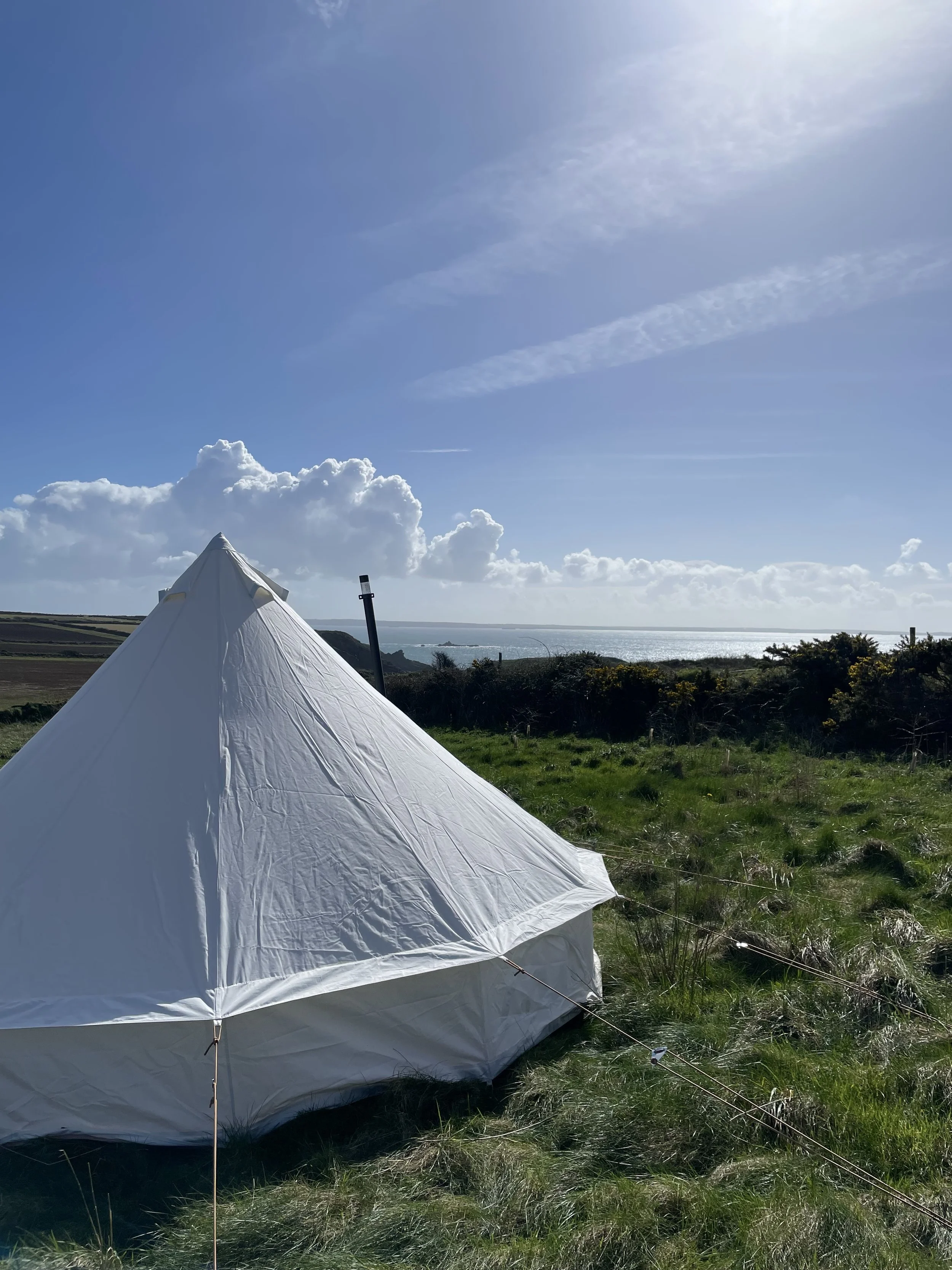 A white tent set up on grassy terrain near the coast with the ocean and a cloudy sky in the background.