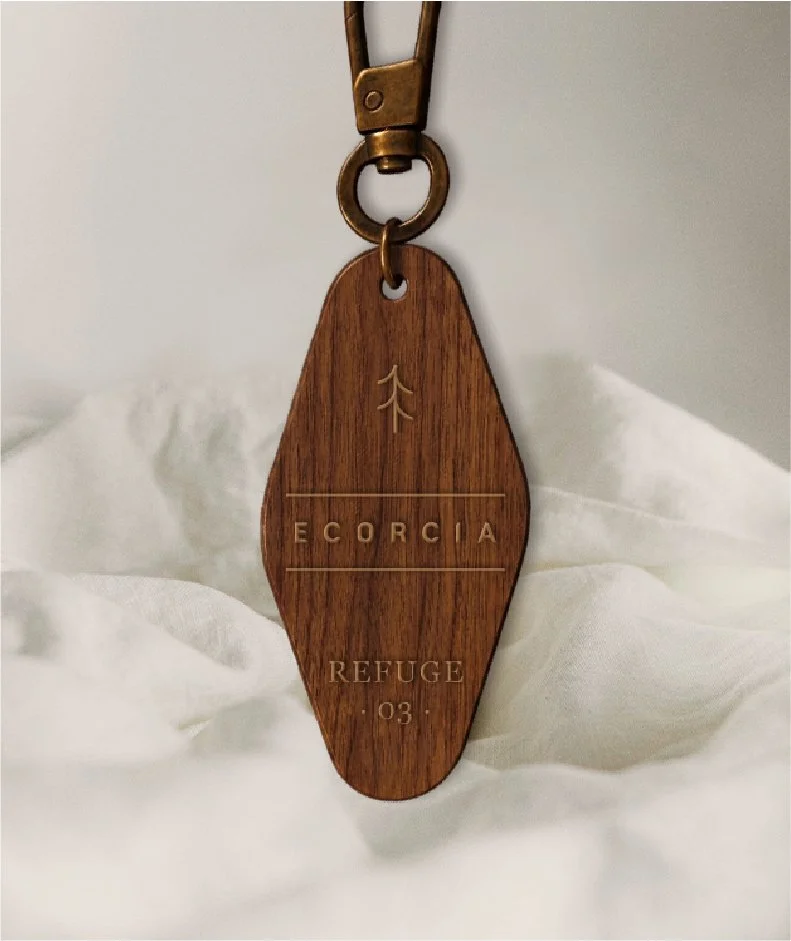 Une clé en bois avec des inscriptions "Ecorcia", "Refuge 03" et un symbole d'arbre, suspendue à un porte-clés en métal