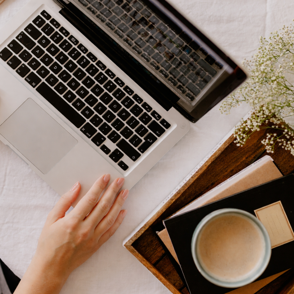 Clavier d'ordinateur portable, main d'une personne, tasse de café, livre, et plante dans un cadre de bureau ou de travail.