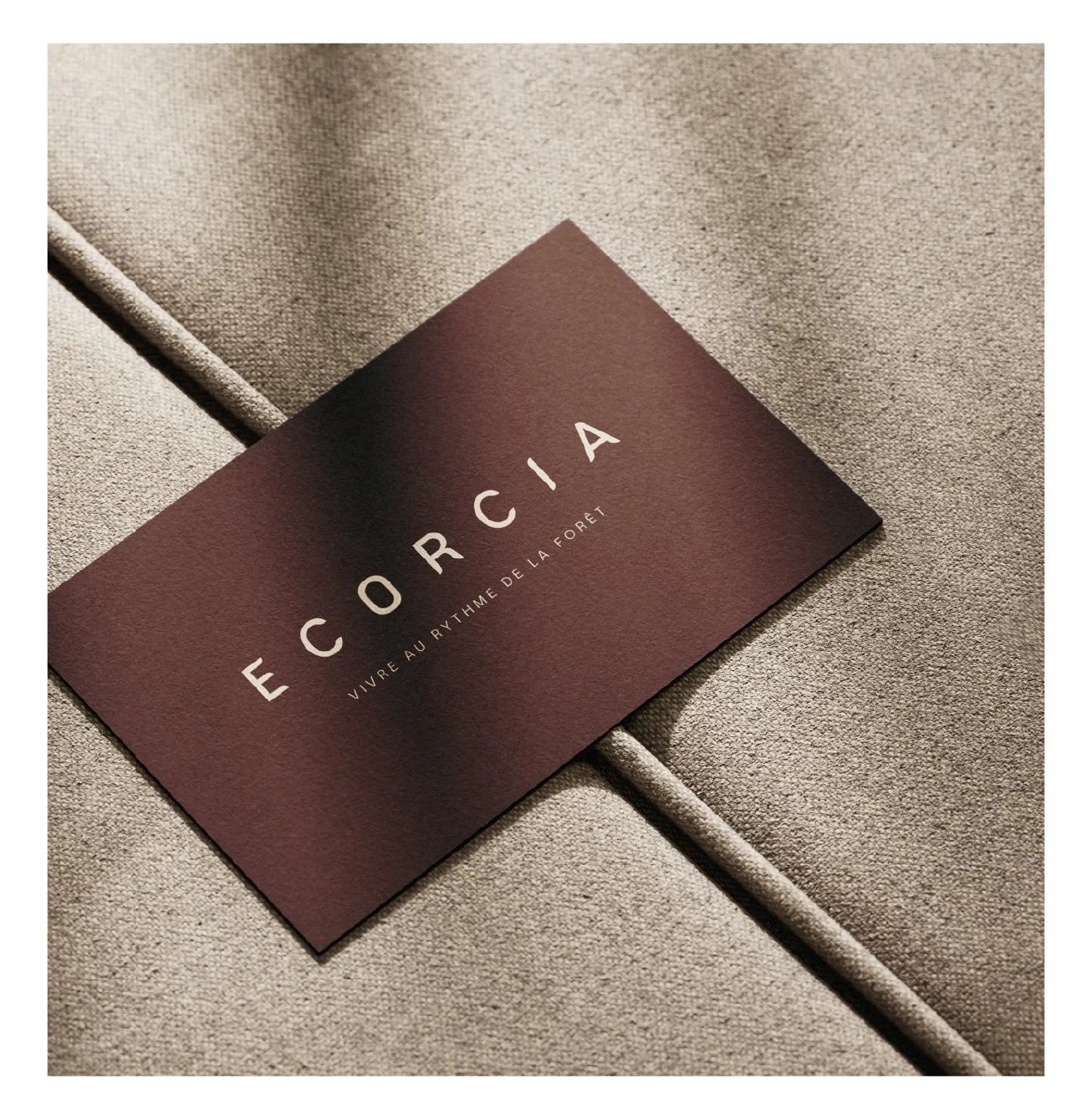 Une carte de visite marron avec le texte 'Ecorcia' et 'Vivre au rythme de la forêt' posée sur un tissu beige.