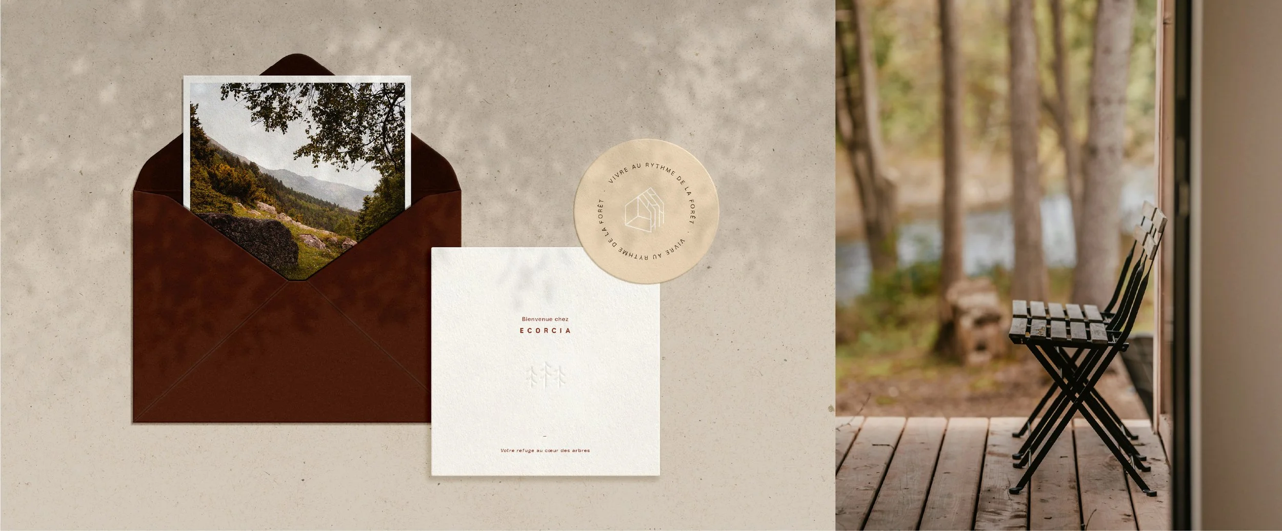 Une enveloppe en cuir marron contenant une photographie d'une forêt montagneuse. À côté, un papier blanc avec du texte en français et une étiquette ronde beige avec un logo et du texte."Vivre au rythme de la forêt" et "Votre refuge au cœur des arbres". À droite, une vue sur un balcon en bois avec deux chaises rabattables noires, donnant sur un paysage forestier avec des arbres et une rivière.