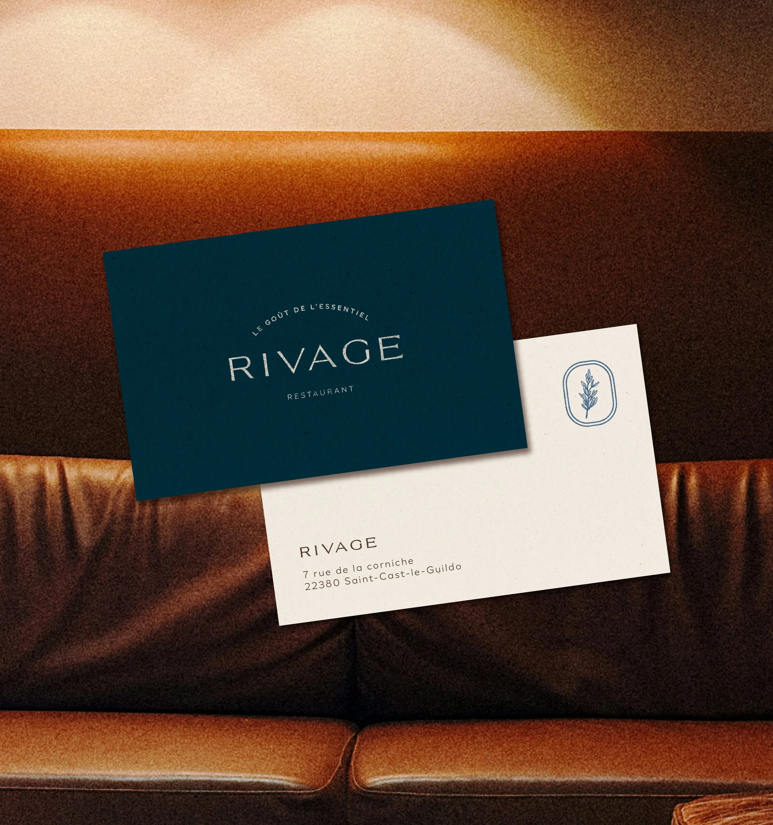 Deux cartes de visite posées sur une surface en bois foncé. La carte en haut à gauche est bleue avec le texte blanc 'RIVAGE' et des mots en français. La carte en bas à droite est blanche avec un symbole d'une branche d'olivier ou de laurier.