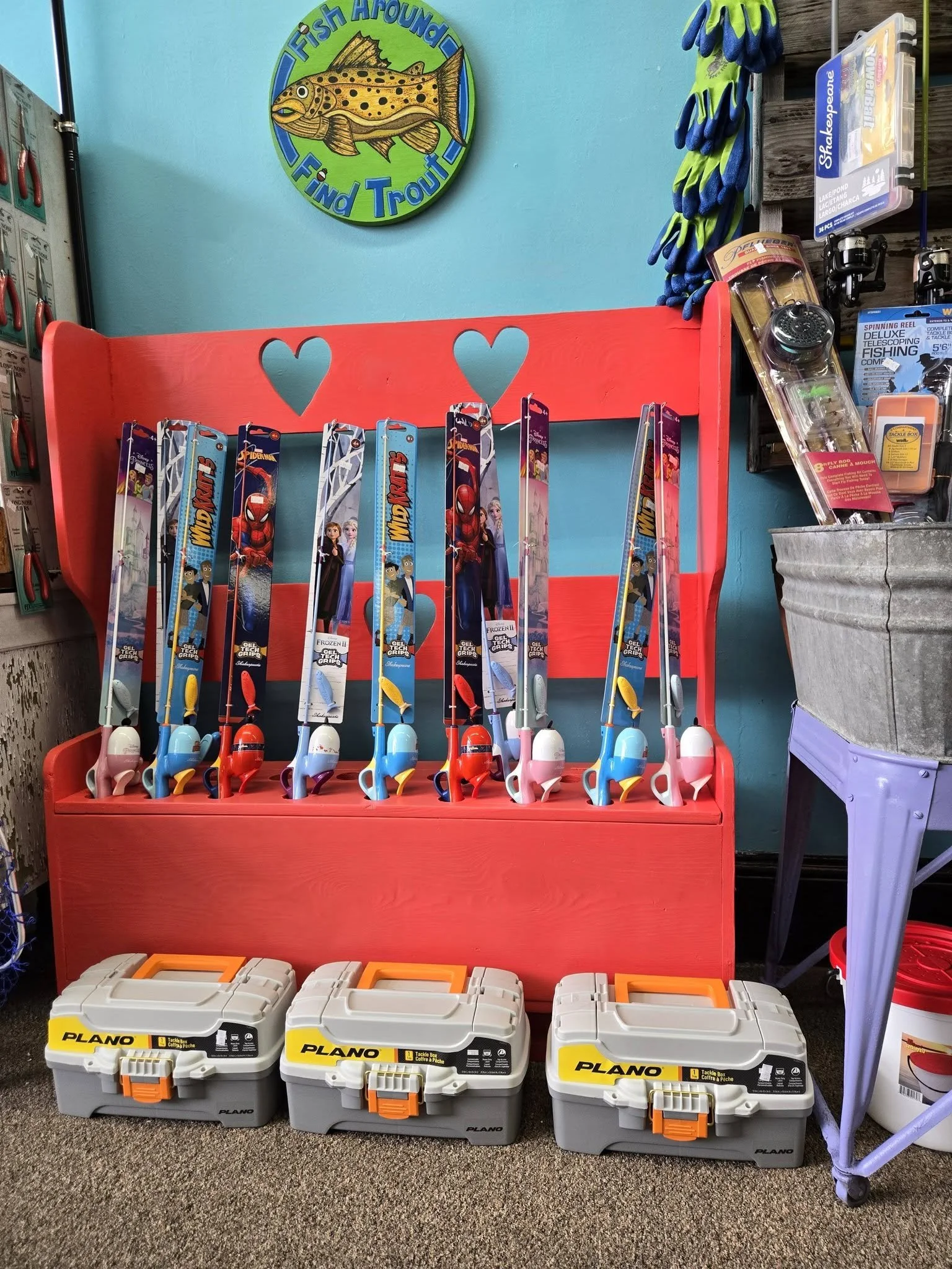 Display of fishing gear at a store, including fishing rods with themed packaging featuring characters from Frozen 2, a red shelving unit, and three Plano tackle boxes in front.