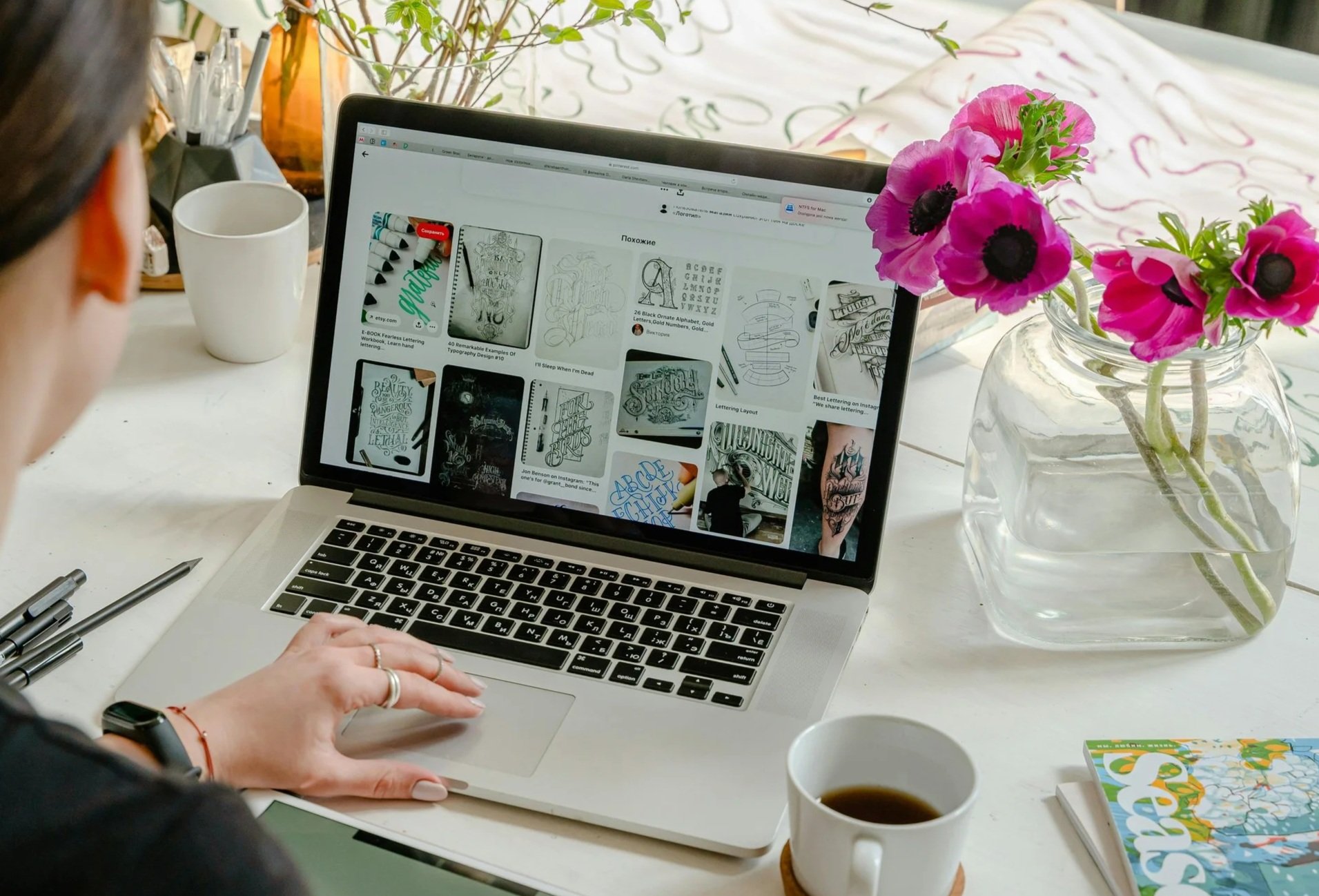 Person working on a laptop at a desk with a potted pink flower and a cup of coffee.