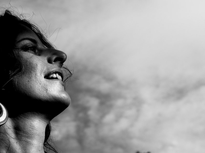 Une femme regarde vers le haut, souriante, sous un ciel nuageux, en noir et blanc.
