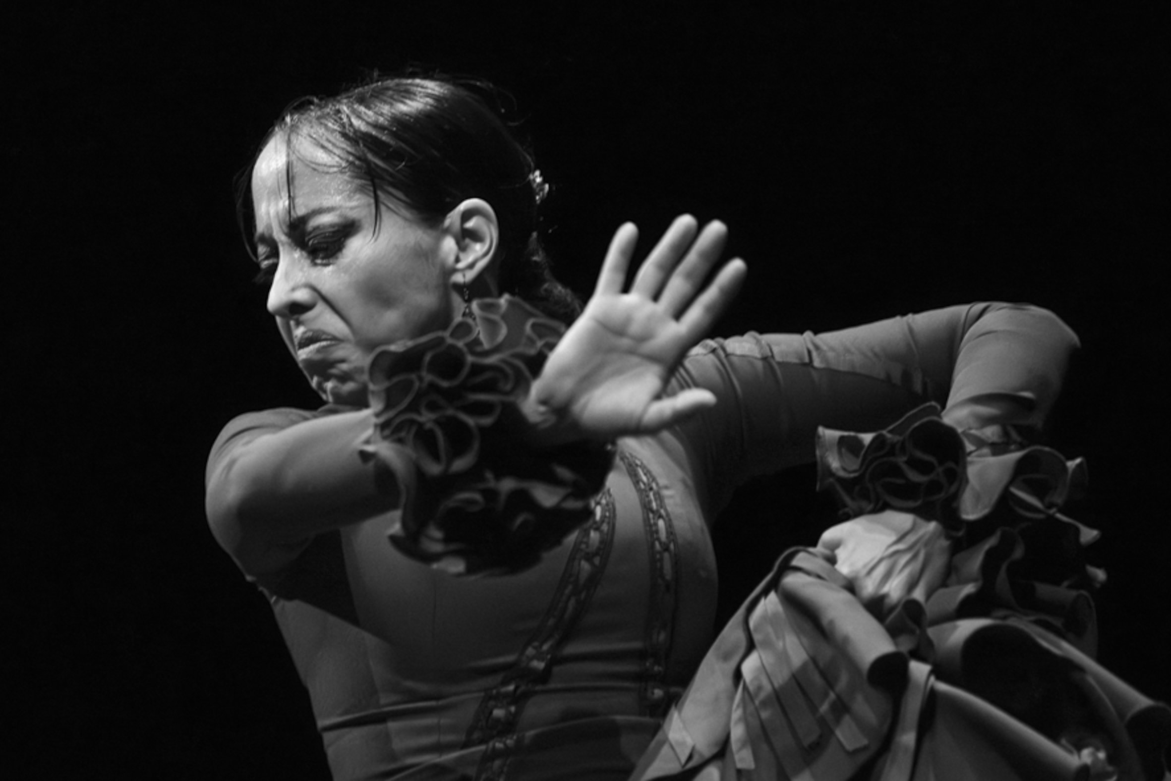 Une femme qui danse ou performe dans un style dramatique, en noir et blanc, avec expression intense, vêtue d'une tenue élégante avec des volants.