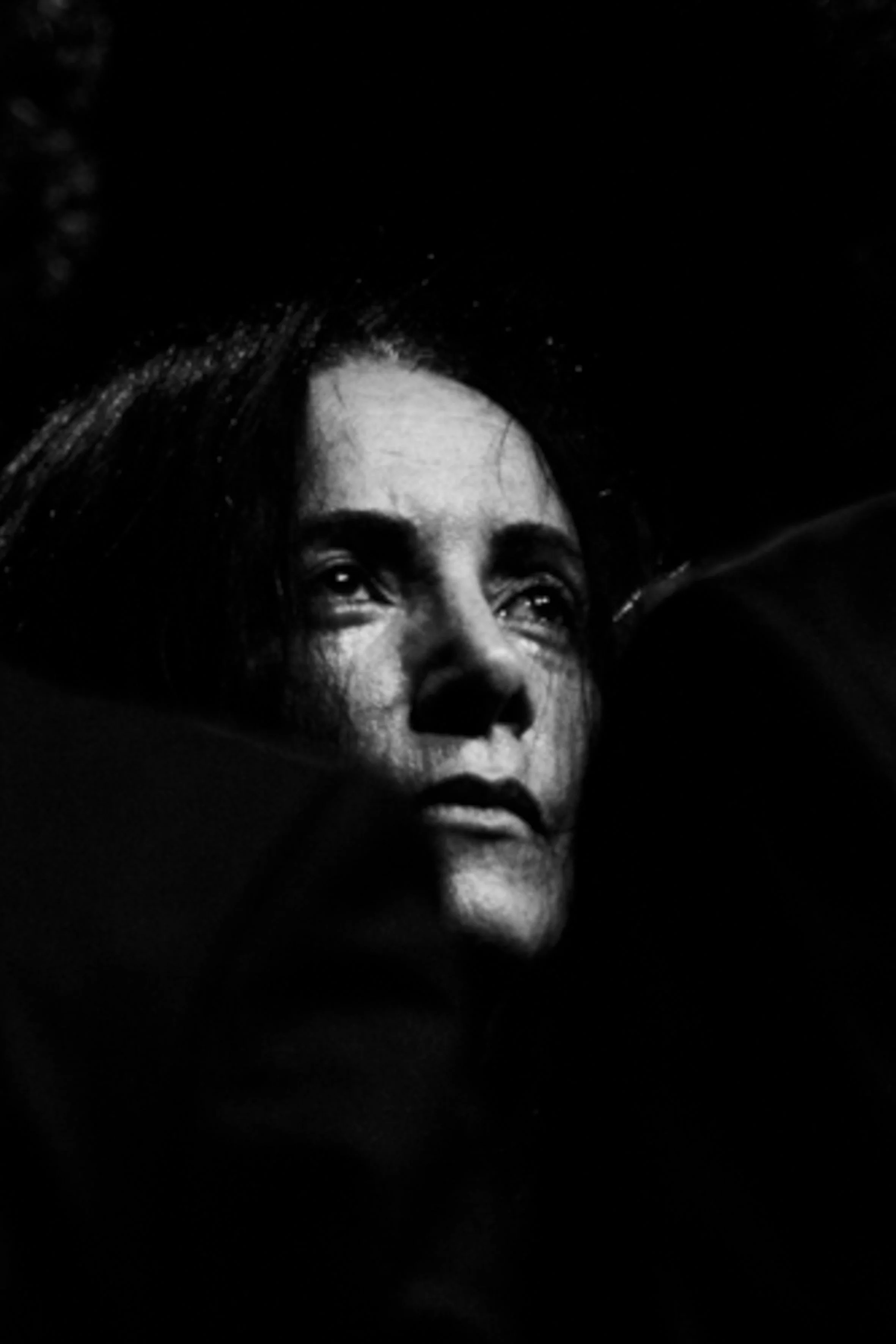 Portrait en noir et blanc d'une femme avec un regard intense, le visage partiellement éclairé, expression sérieuse.