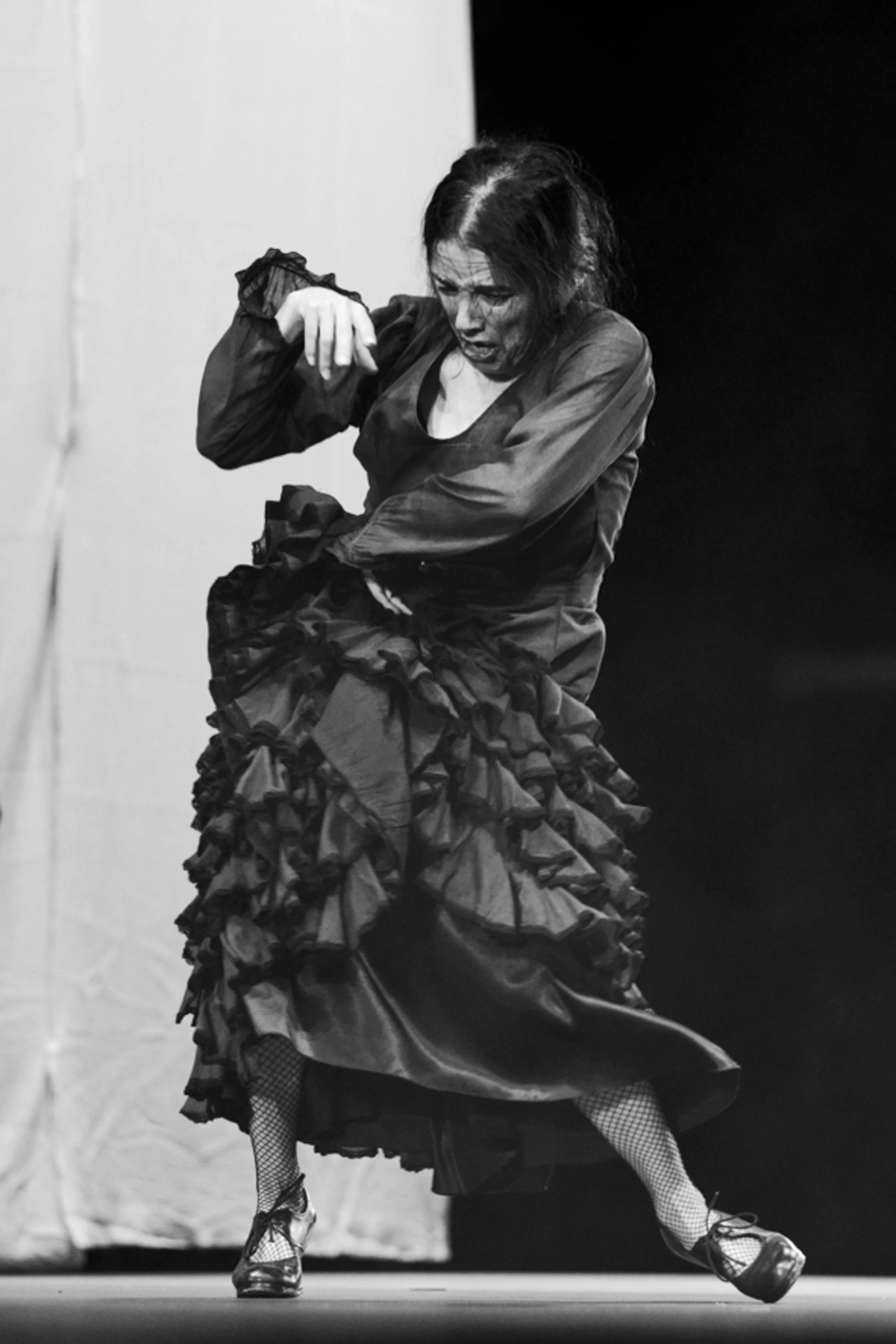 Une femme dans un costume de flamenco en train de danser, vêtue d'une robe à volants et portant des chaussures de danse à talons, en noir et blanc.