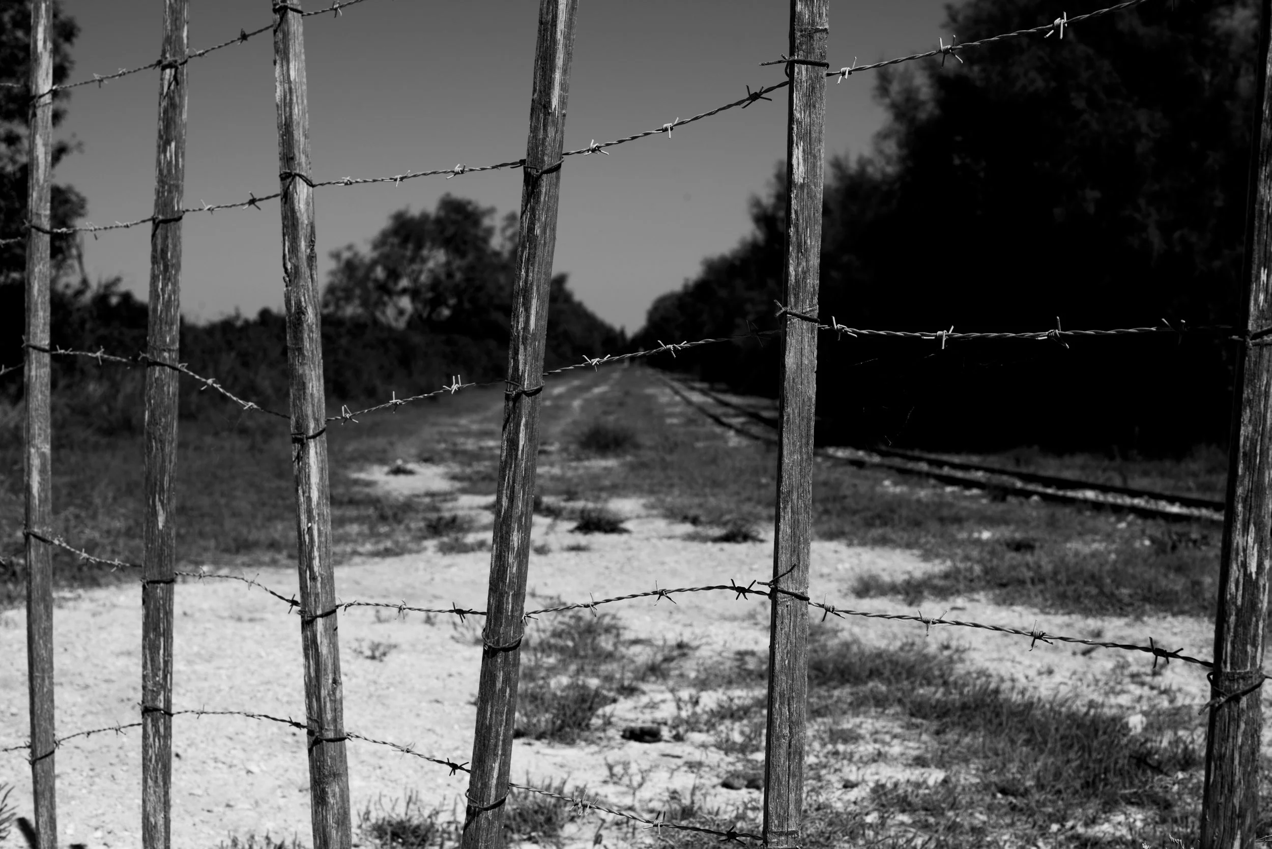 Clôture en bois et fil de fer barbelé à l'entrée d'une voie ferrée dans un paysage rural.