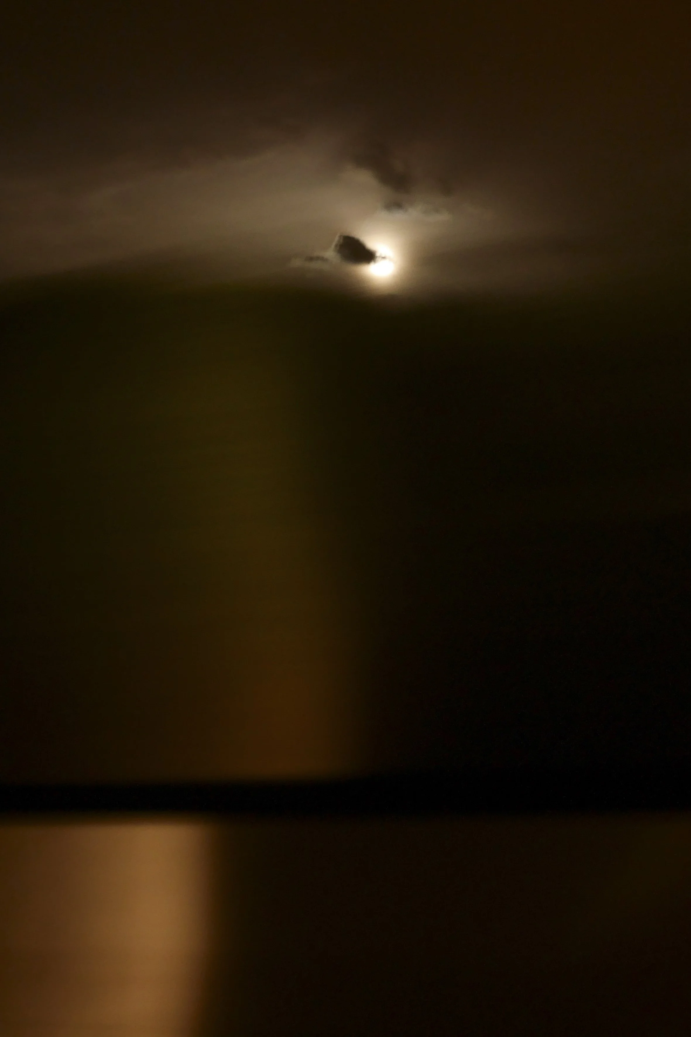 Une lune partiellement couverte par des nuages la nuit, avec un ciel sombre.