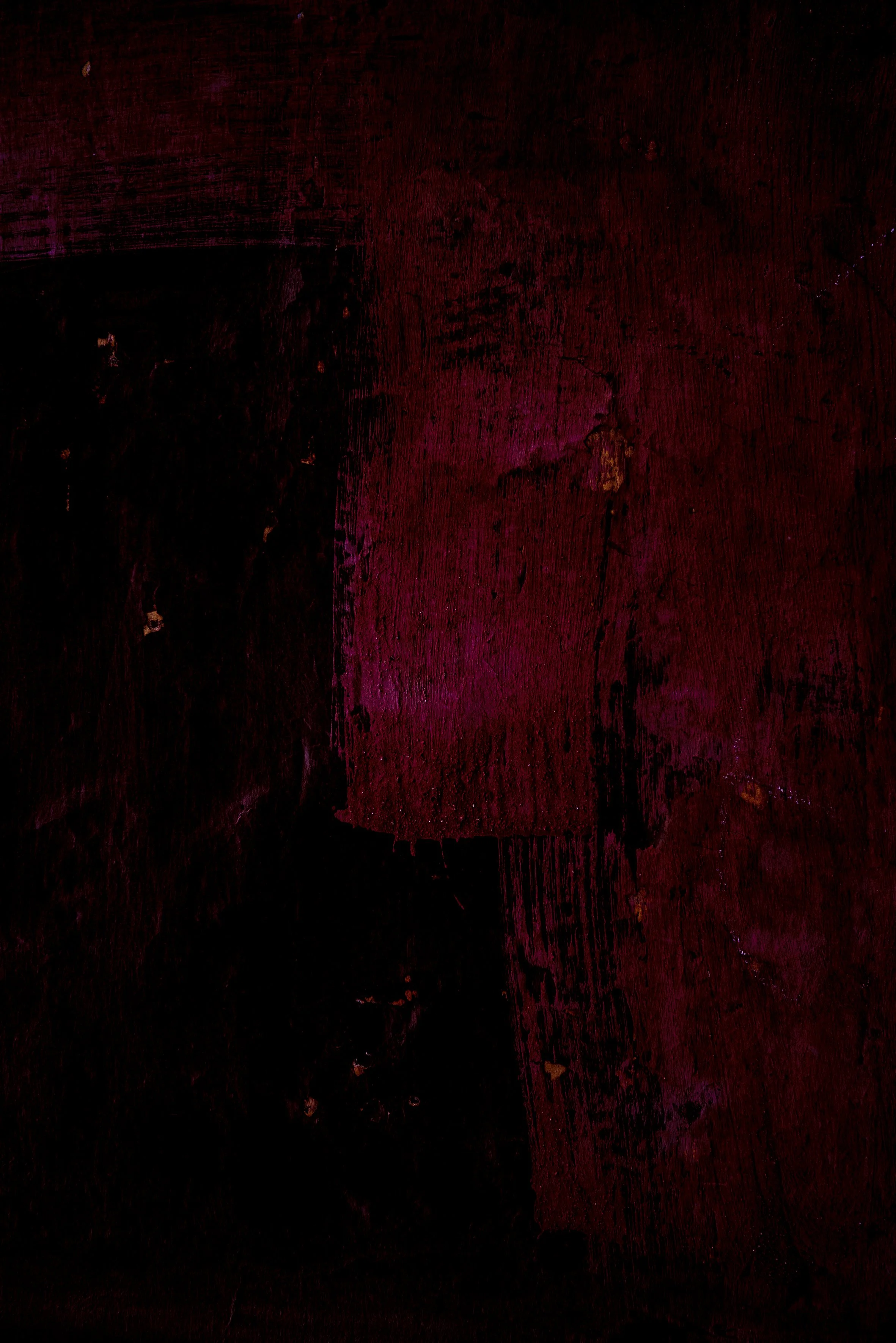 Surface en bois sombre avec taches de couleur rouge et rose.