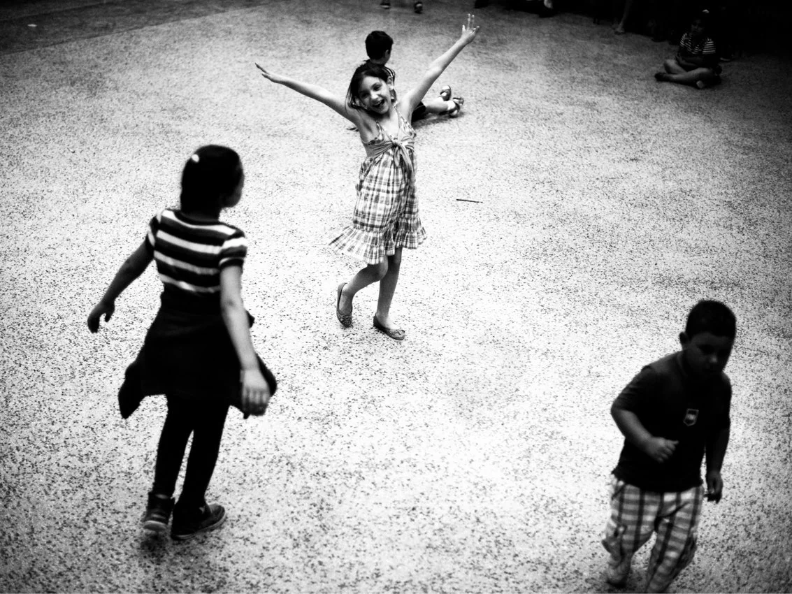 Quatre enfants jouent dans une pièce, dont une fille souriante avec les bras levés.